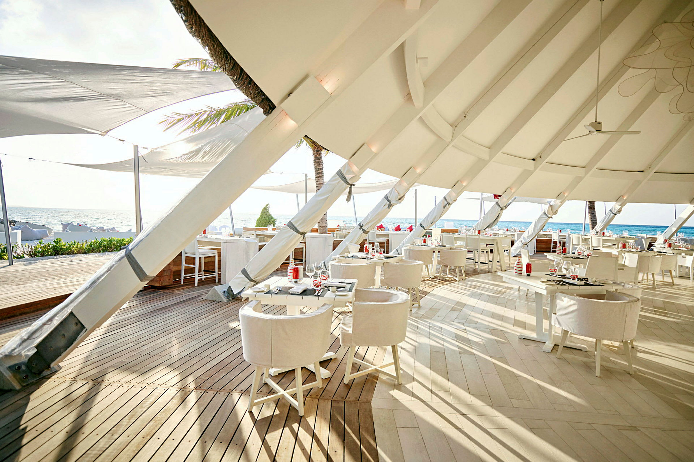 Restaurant med moderne hvite møbler og takduk ved stranden. (AI-generert tekst)