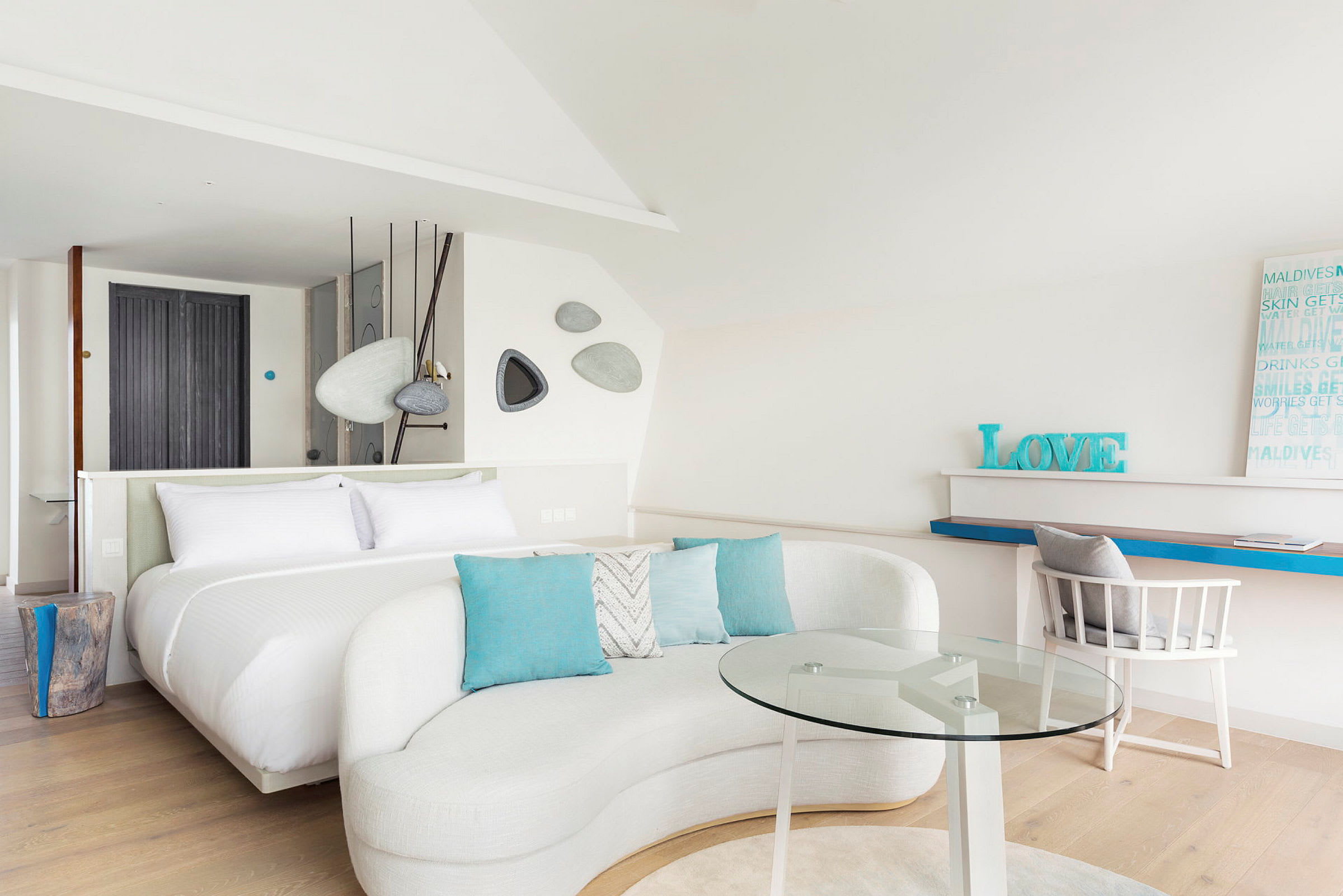 Et moderne og lyst hotellrom med en stor seng, sofagruppe med glassbord og arbeidsområde. (AI-generert tekst)
