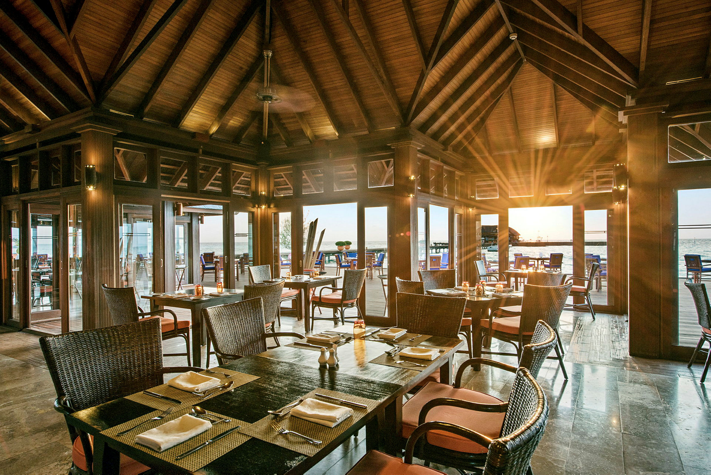 Restaurant med treinteriør og dekkede bord, med utsikt mot havet gjennom glasspartier. (AI-generert tekst)