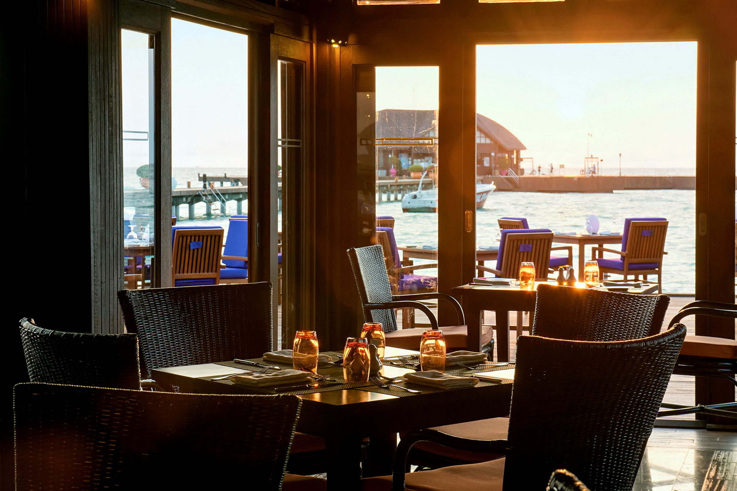Restaurant med bord og stoler inne samt havutsikt fra vinduer. (AI-generert tekst)