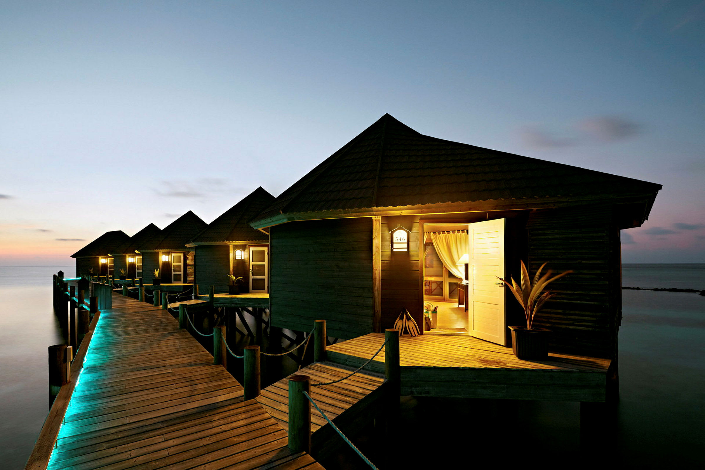 Sjøbungalower på en brygge med kveldsbelysning. (AI-generert tekst)