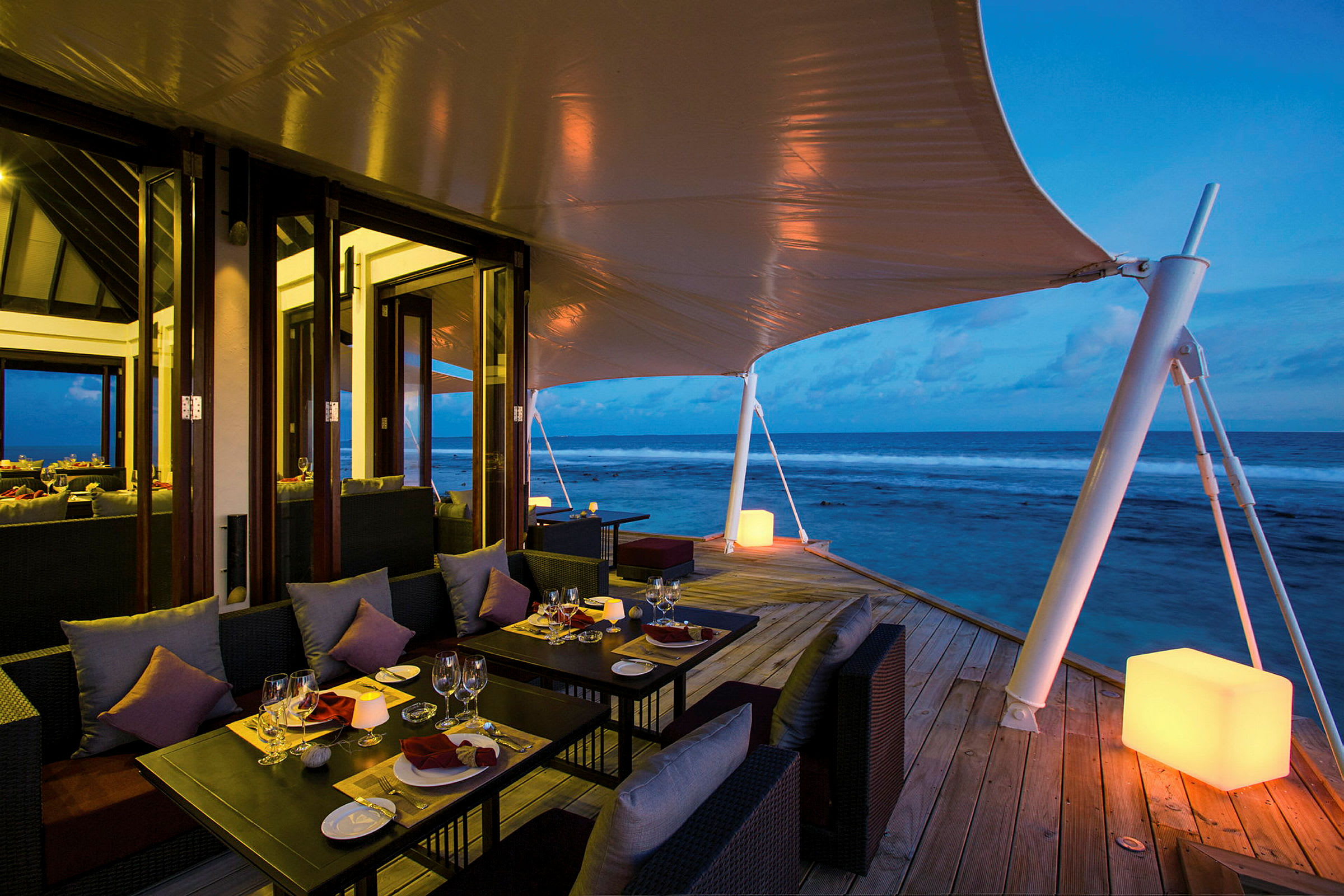 Terrasse med spisebord og sofaer ved havet om kvelden. (AI-generert tekst)