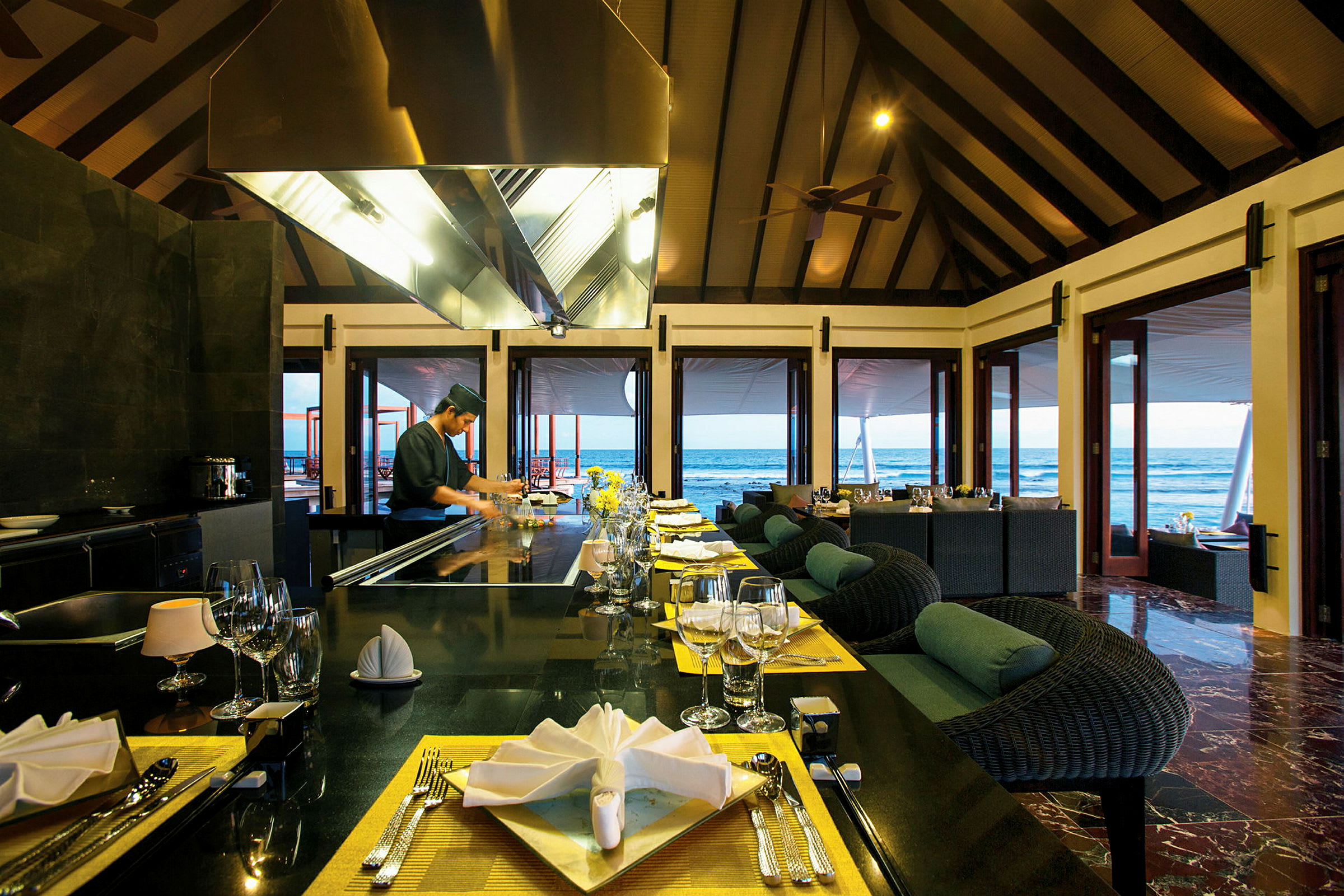 Restaurant ved havet med dekkede bord og åpne dører mot utsikten. (AI-generert tekst)