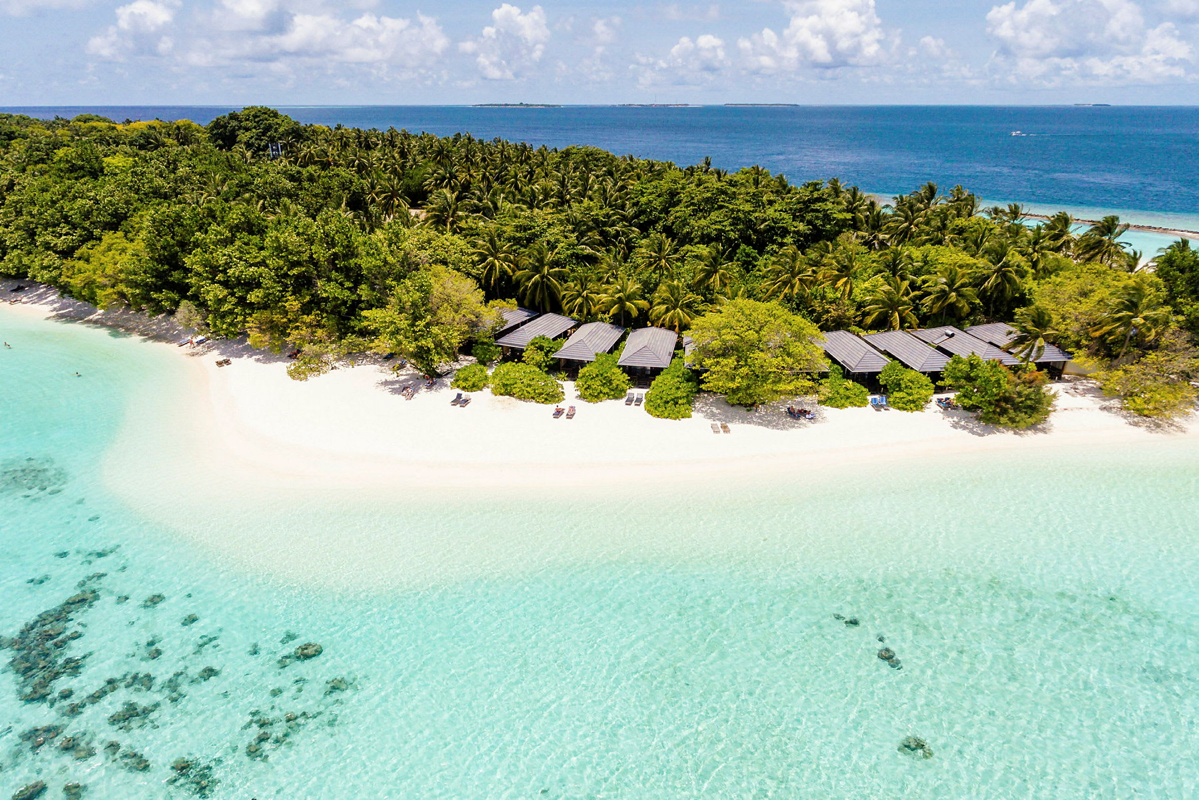 En tropisk strand med klart turkis vann, bungalower og tett vegetasjon. (AI-generert tekst)