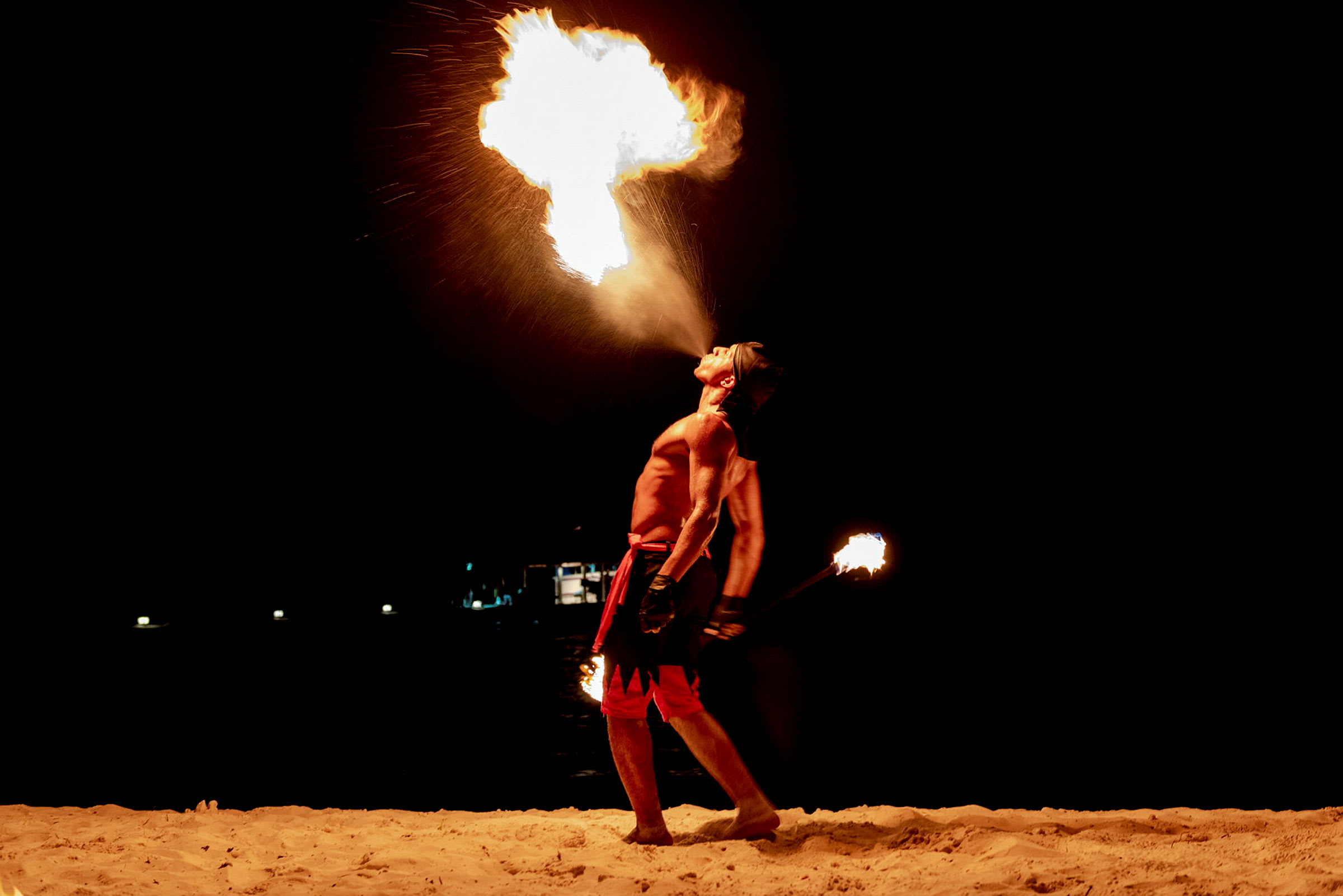 En person utfører et flammeshow på en sandstrand om natten. (AI-generert tekst)
