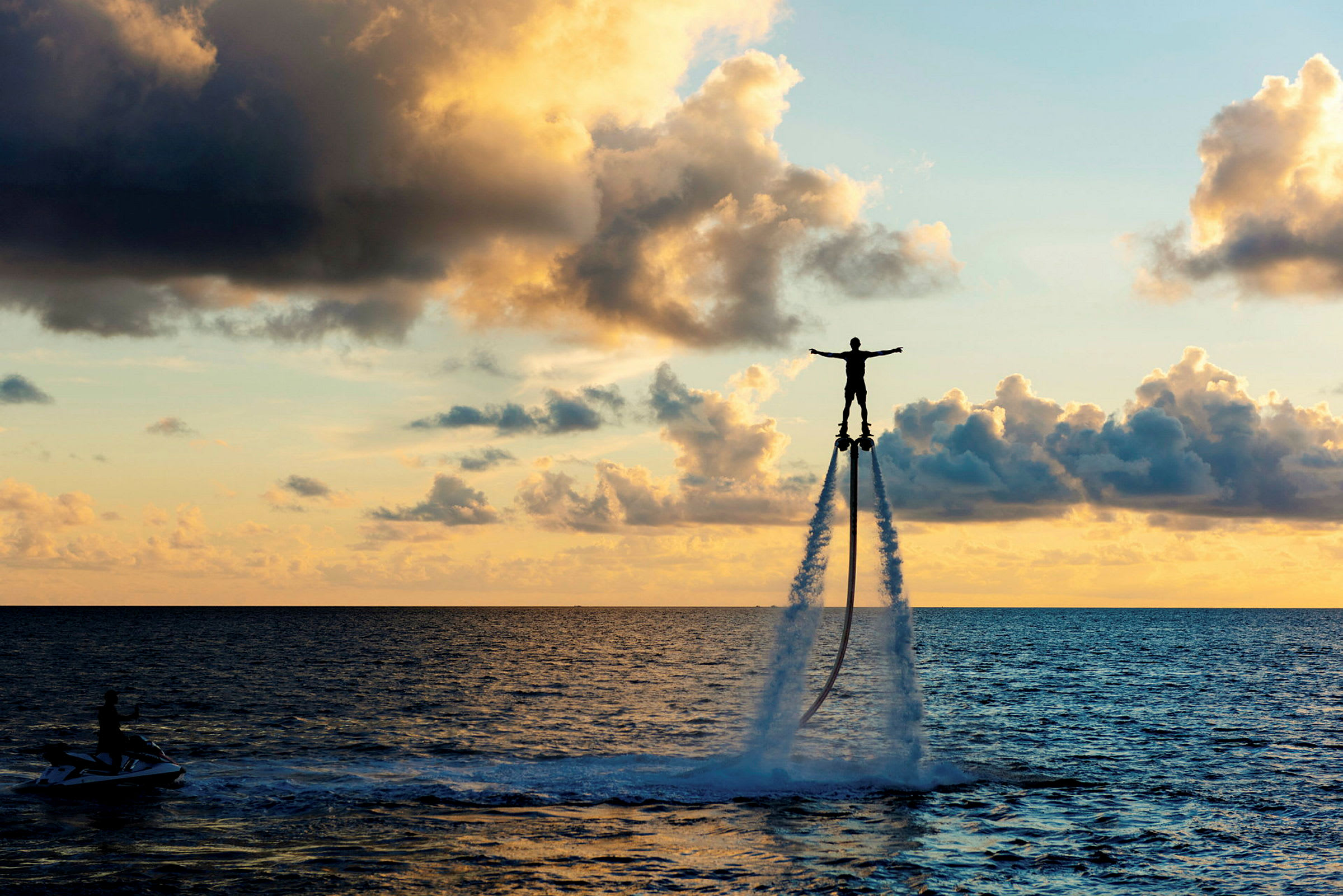 En person flyr over havet ved hjelp av en vannjetpack mens solen går ned. (AI-generert tekst)