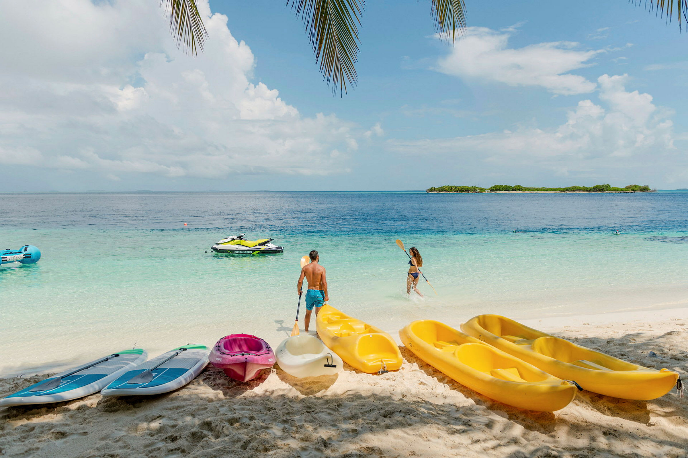 Personer på stranden med kajakker og paddleboards samt vannscooter på havet. (AI-generert tekst)
