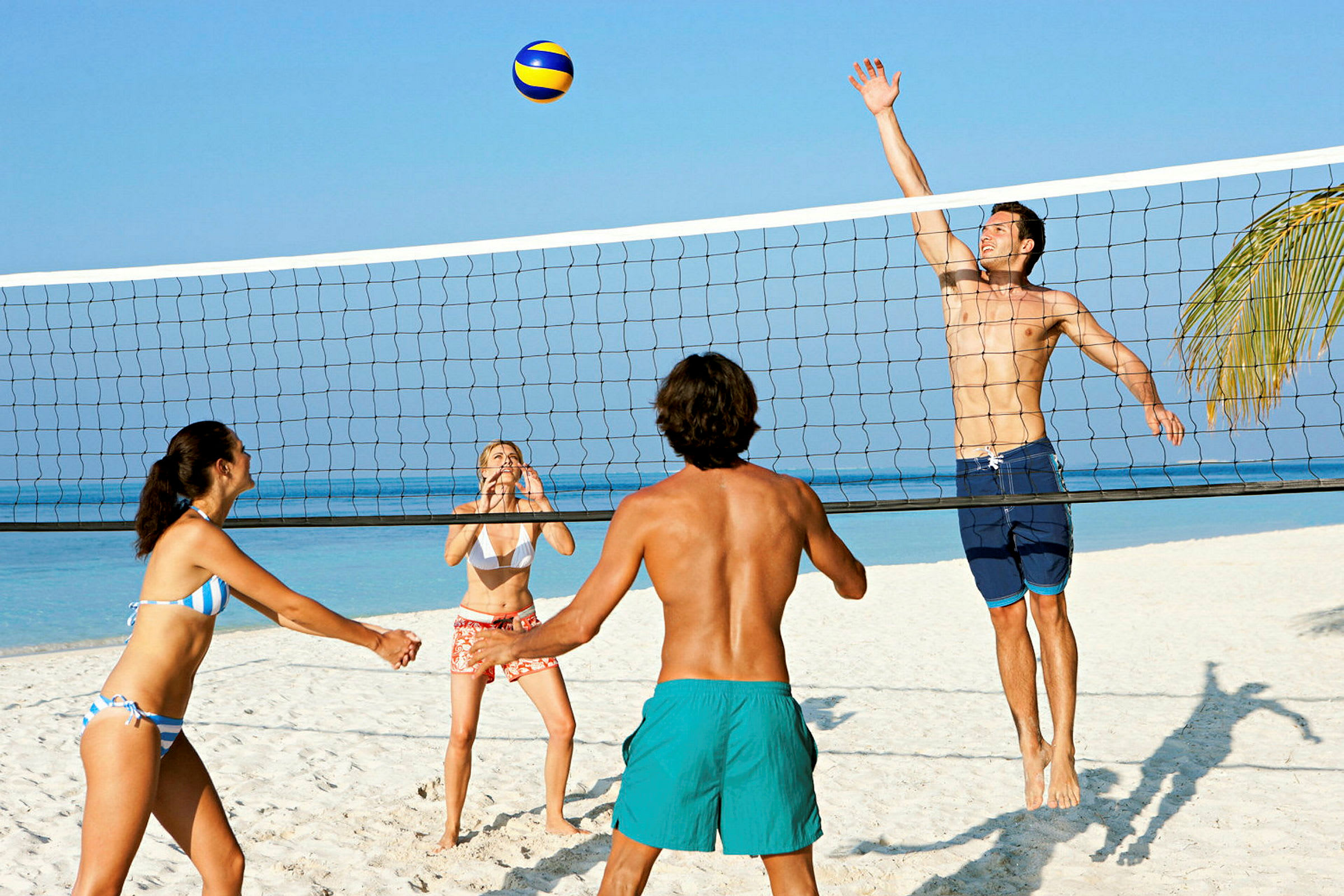 Fire personer spiller sandvolleyball på en strand nær havet. (AI-generert tekst)