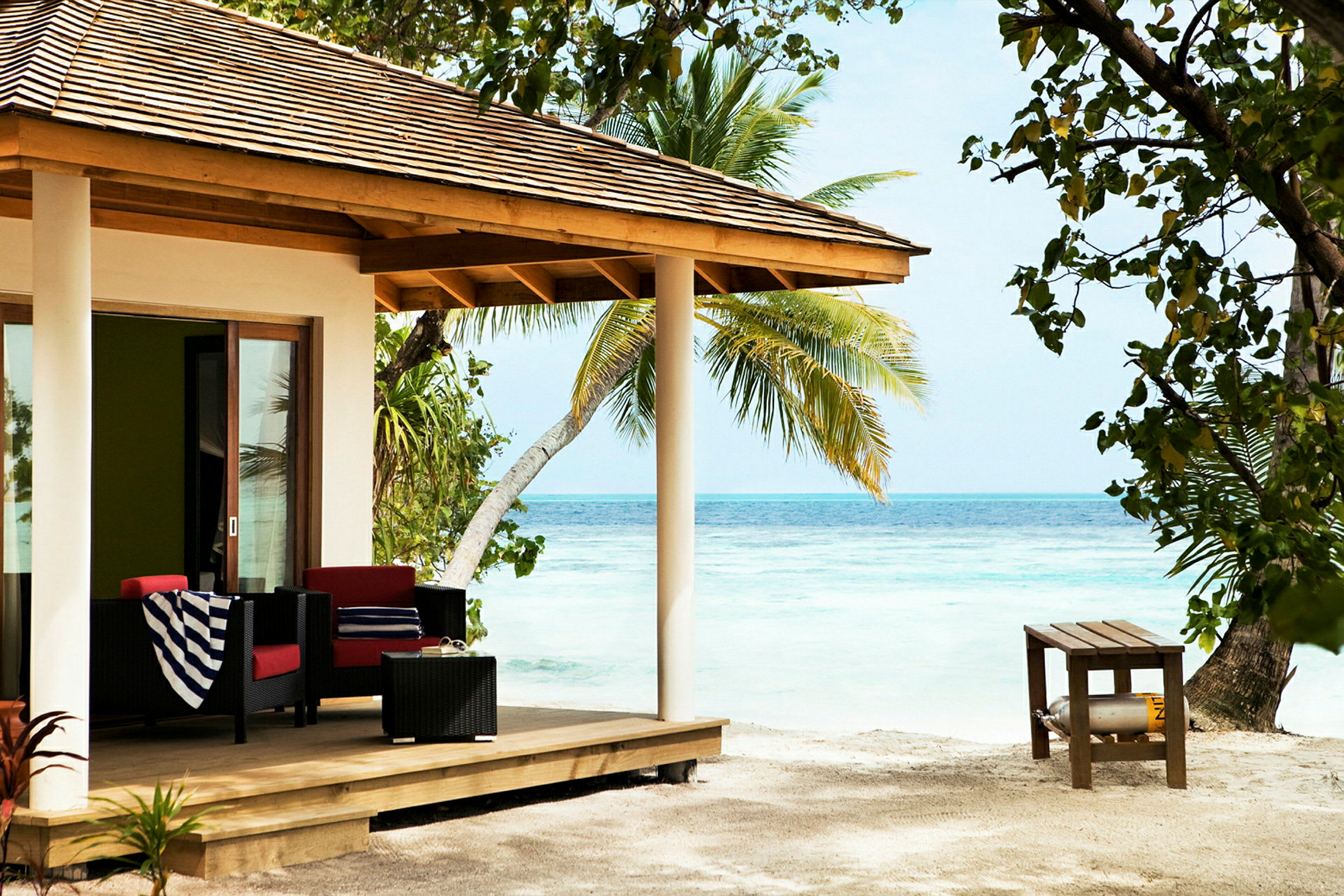 Strandvilla med veranda møblert med sofaer, bord og dekorert med palmer rundt. (AI-generert tekst)