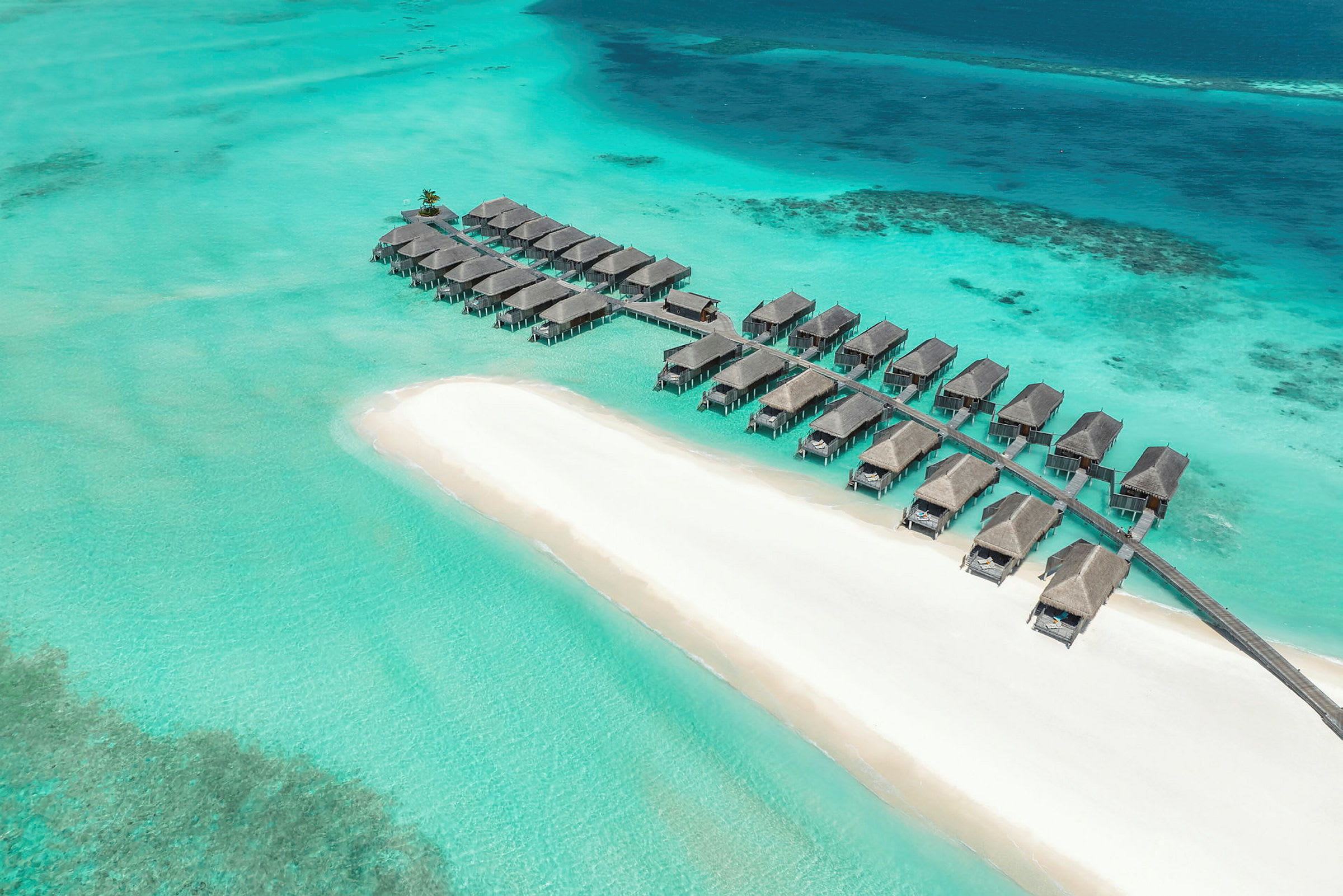 Bungalower på pæler over klart turkist vann ved en hvit sandstrand. (AI-generert tekst)