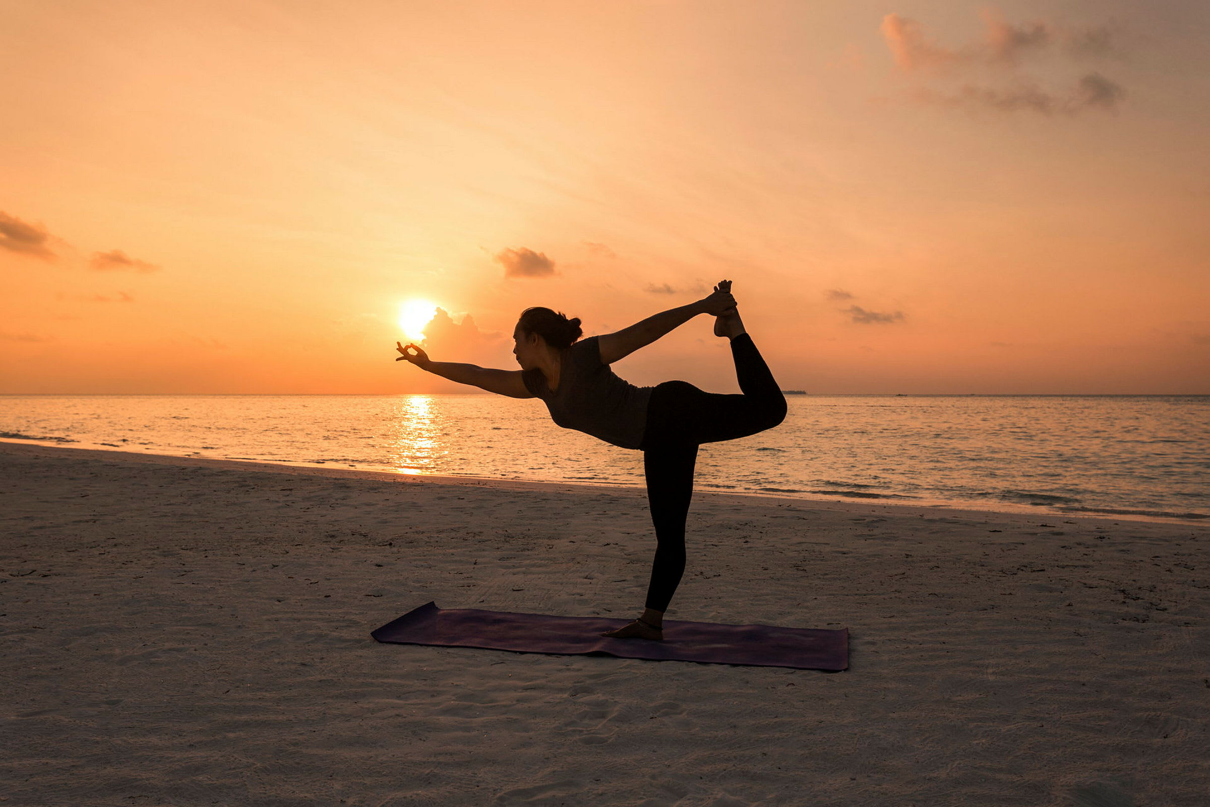 Silhuetten av en person som utøver yoga ved stranden under solnedgangen. (AI-generert tekst)
