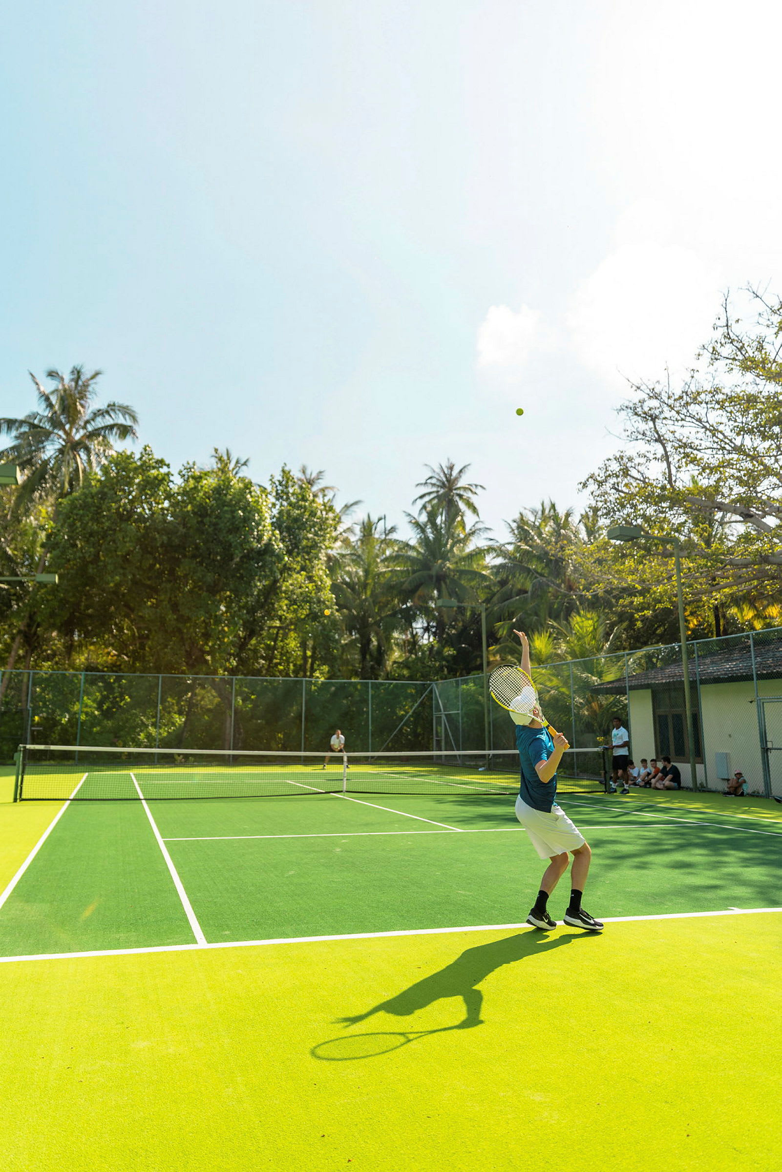En person spiller tennis på en utendørsbane omgitt av trær. (AI-generert tekst)