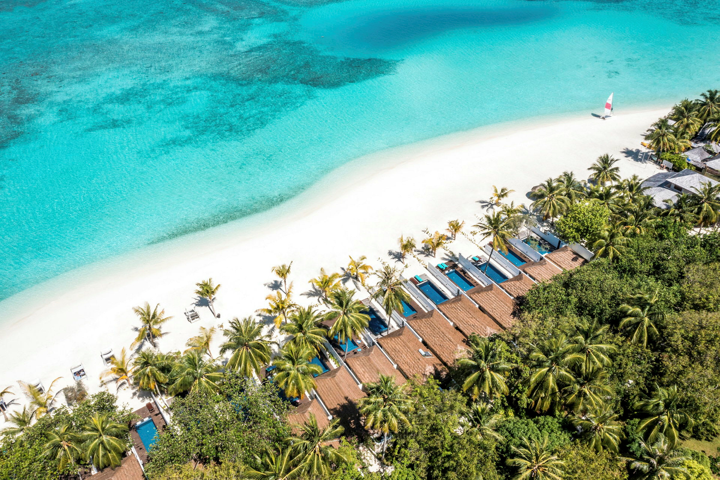 Luftfoto av en tropisk strand med hvit sand, turkis hav, palmer og private bungalower med bassenger. (AI-generert tekst)