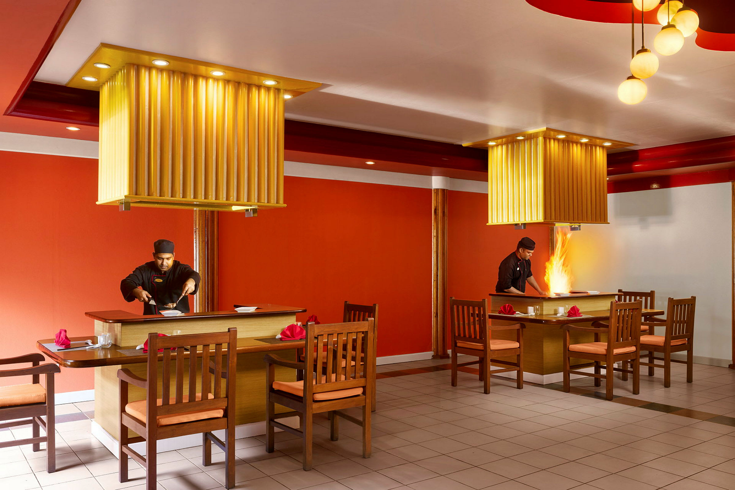 To spisebord med tilhørende stoler i en restaurant med oransje interiør og taklamper. (AI-generert tekst)