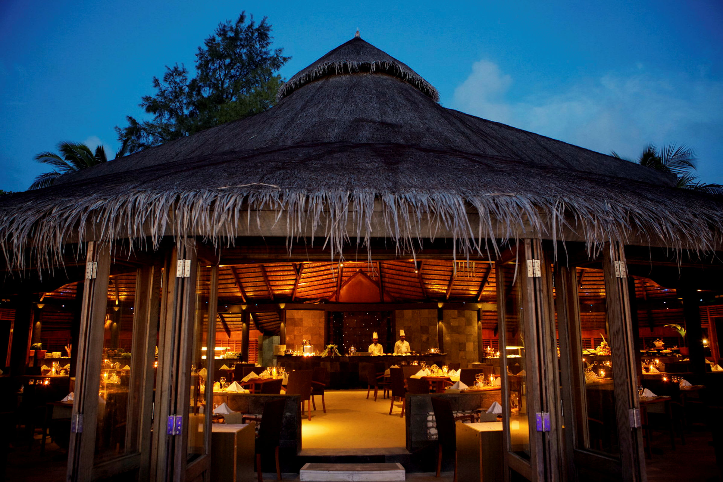 Restaurant med stråtak opplyst av varme lys om kvelden. (AI-generert tekst)