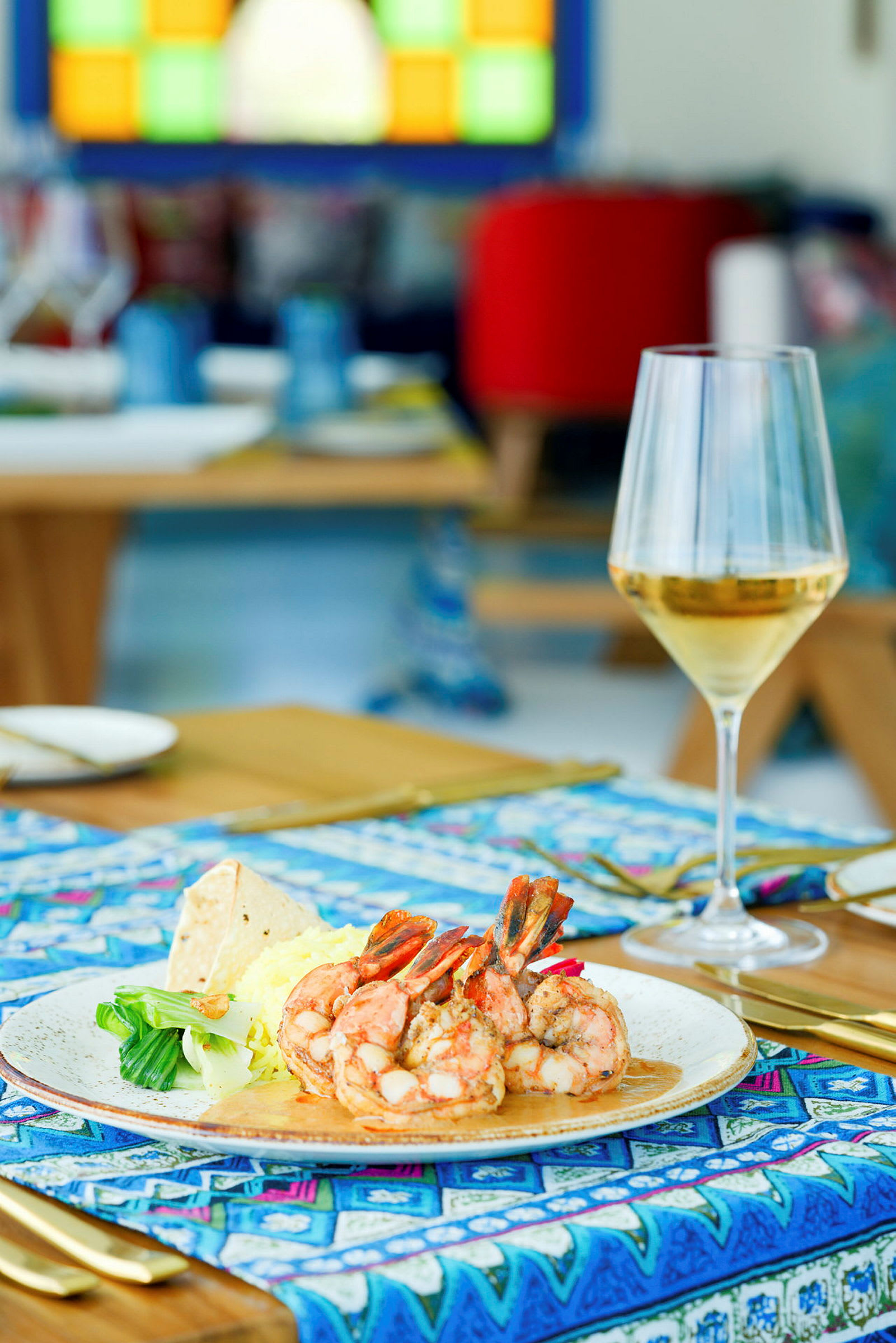 En tallerken med reker, grønnsaker og ris samt et glass vin på et dekket bord. (AI-generert tekst)
