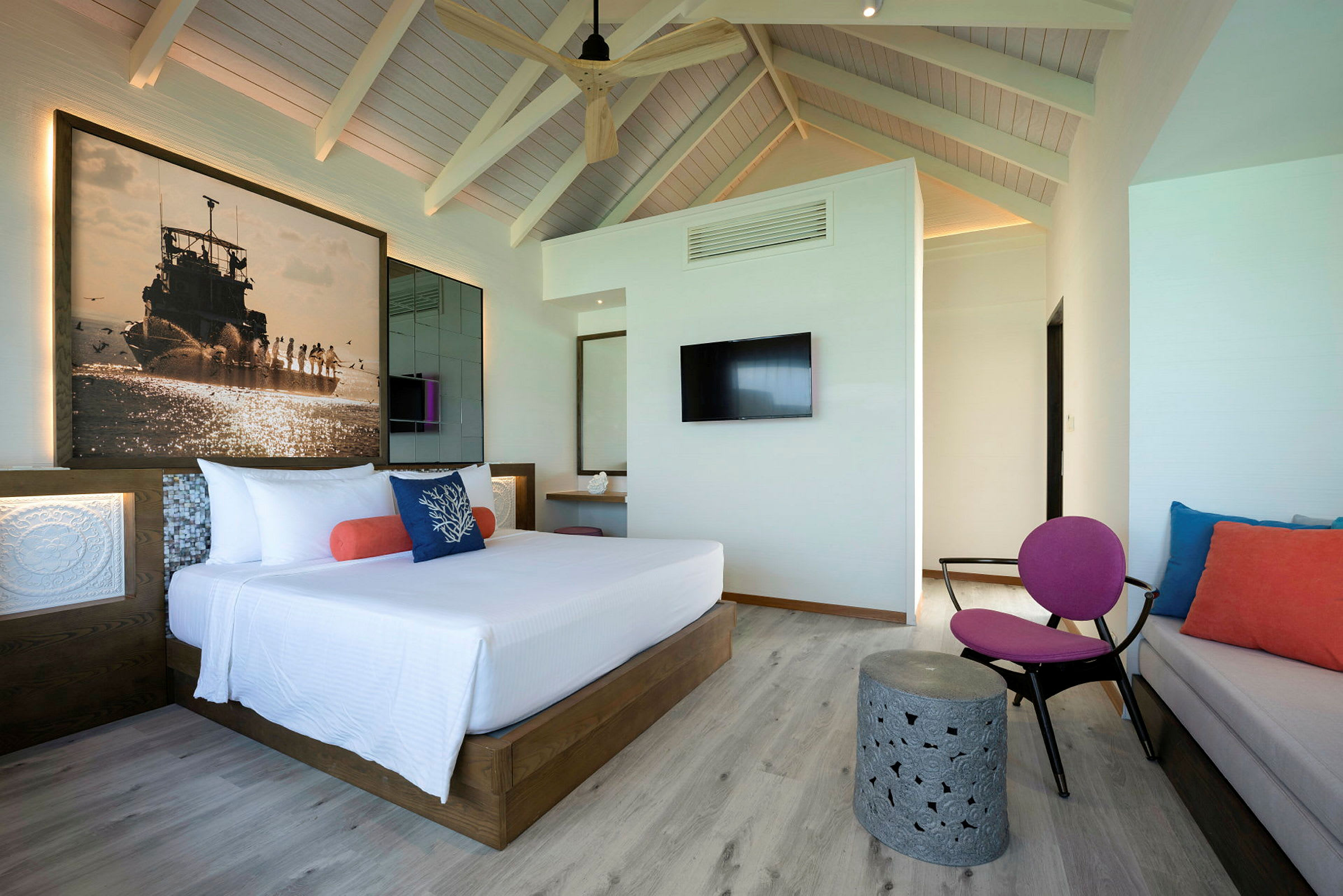 Et moderne hotellrom med en stor seng, fargerike puter og en veggmontert TV. (AI-generert tekst)