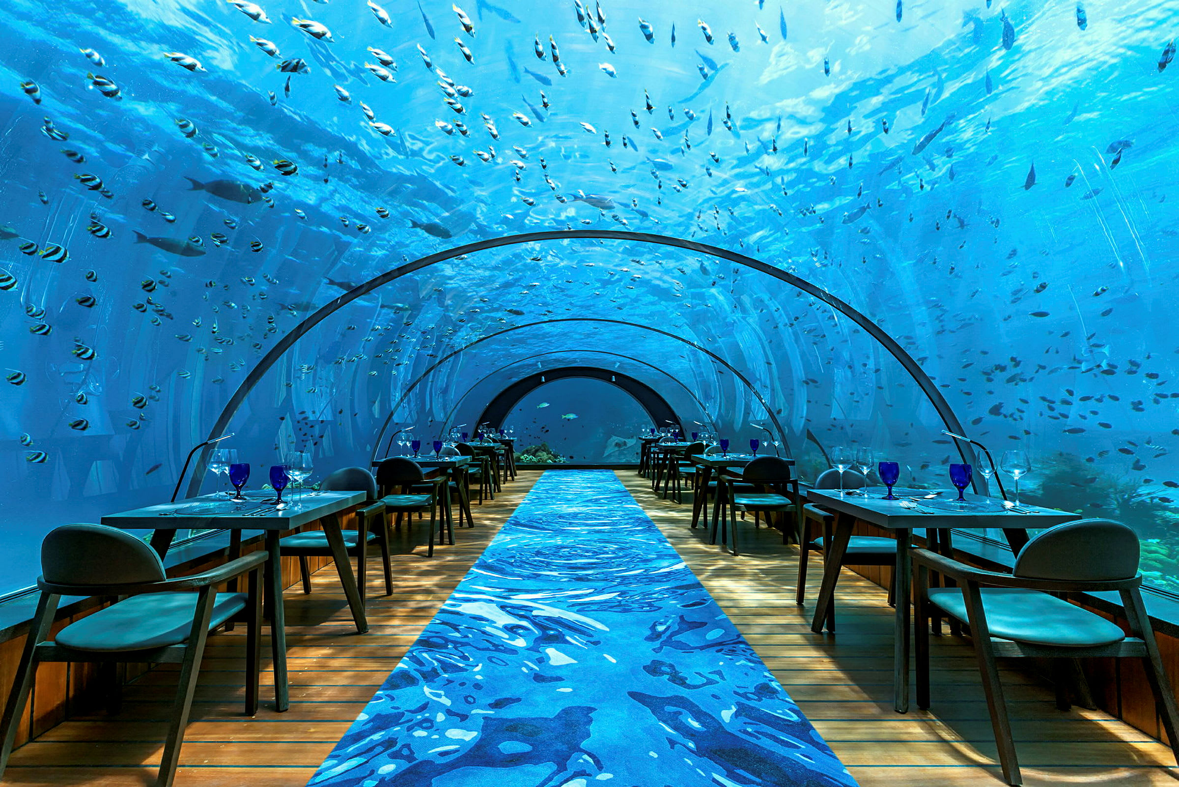 Undervannsrestaurant med glassvegger omgitt av fisk. (AI-generert tekst)