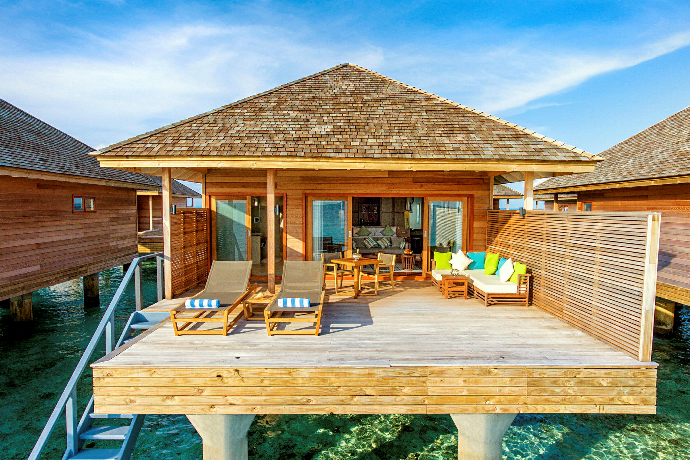 En overwater-bungalow med treterrasse og sittemøbler. (AI-generert tekst)