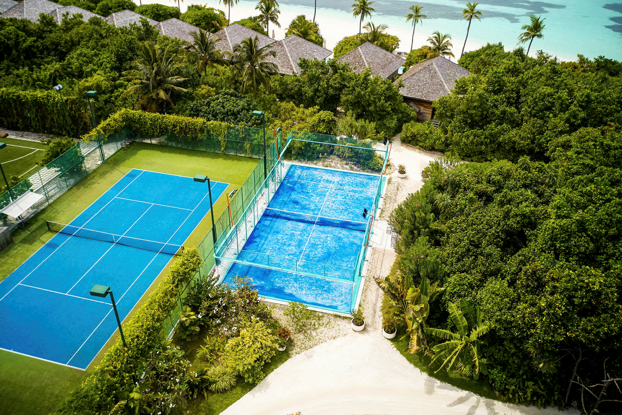 To tennisbaner blant grønne omgivelser nær stranden. (AI-generert tekst)