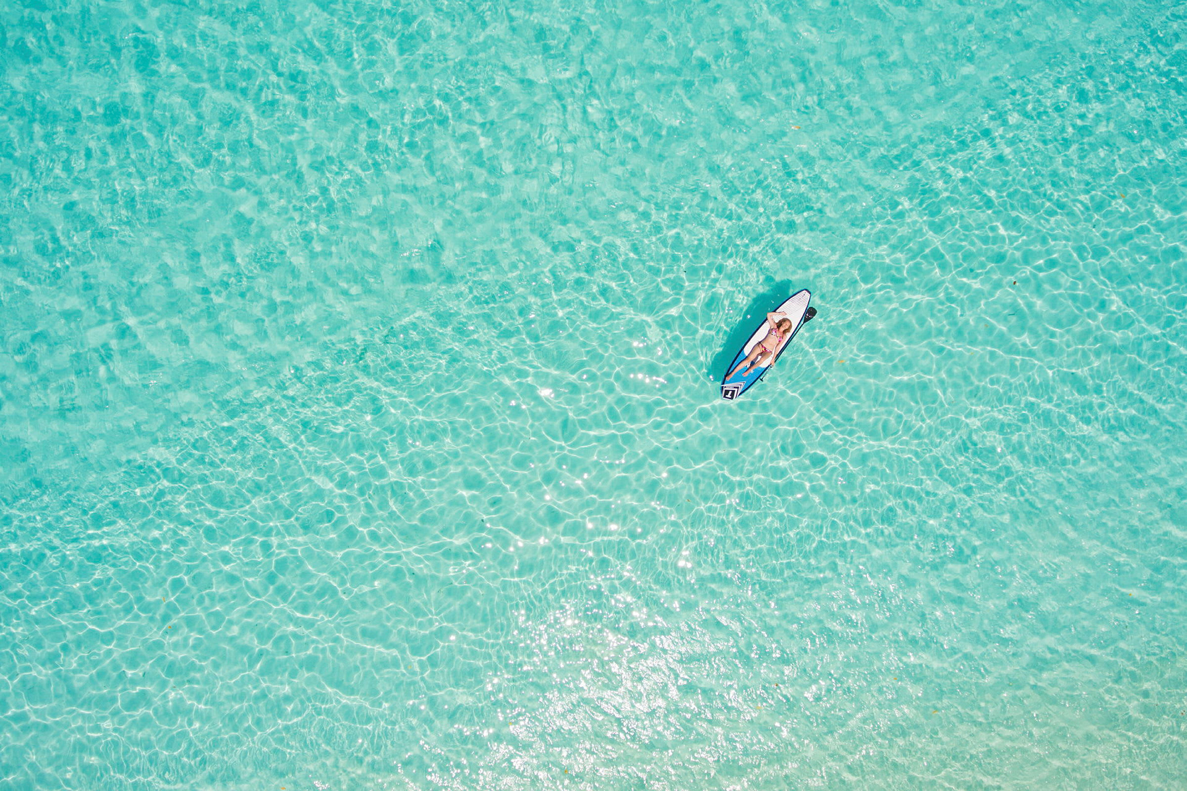 En person ligger på en paddleboard på klart turkist vann. (AI-generert tekst)