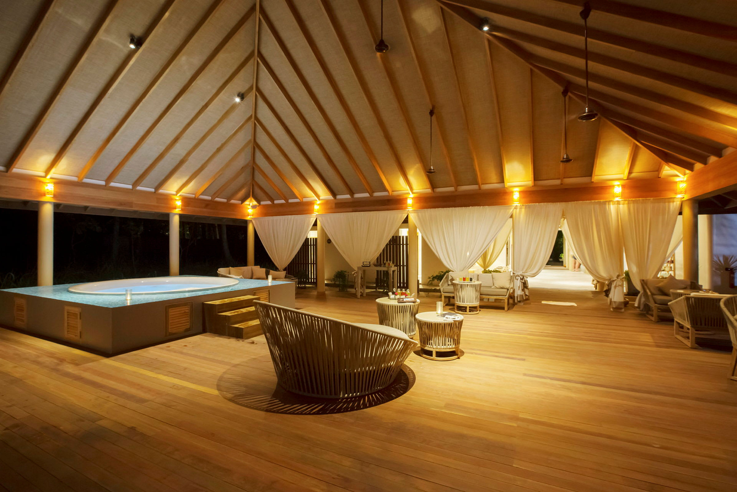 En luksuriøs utendørs lounge med basseng og tremøbler, opplyst om kvelden. (AI-generert tekst)