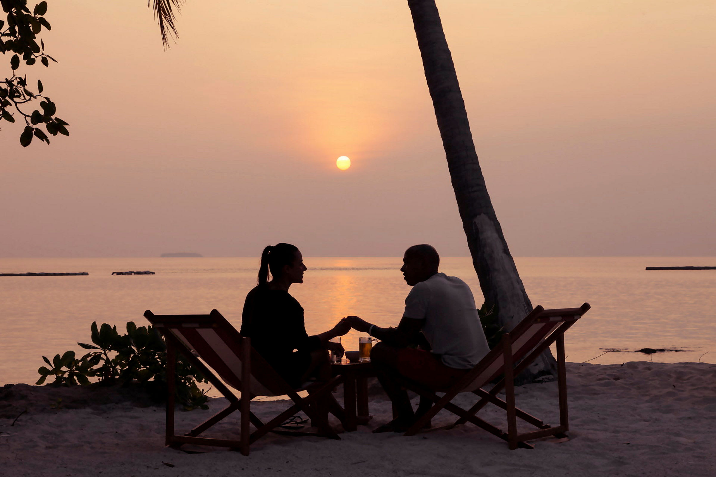 Et par sitter på strandstoler ved stranden under en solnedgang. (AI-generert tekst)