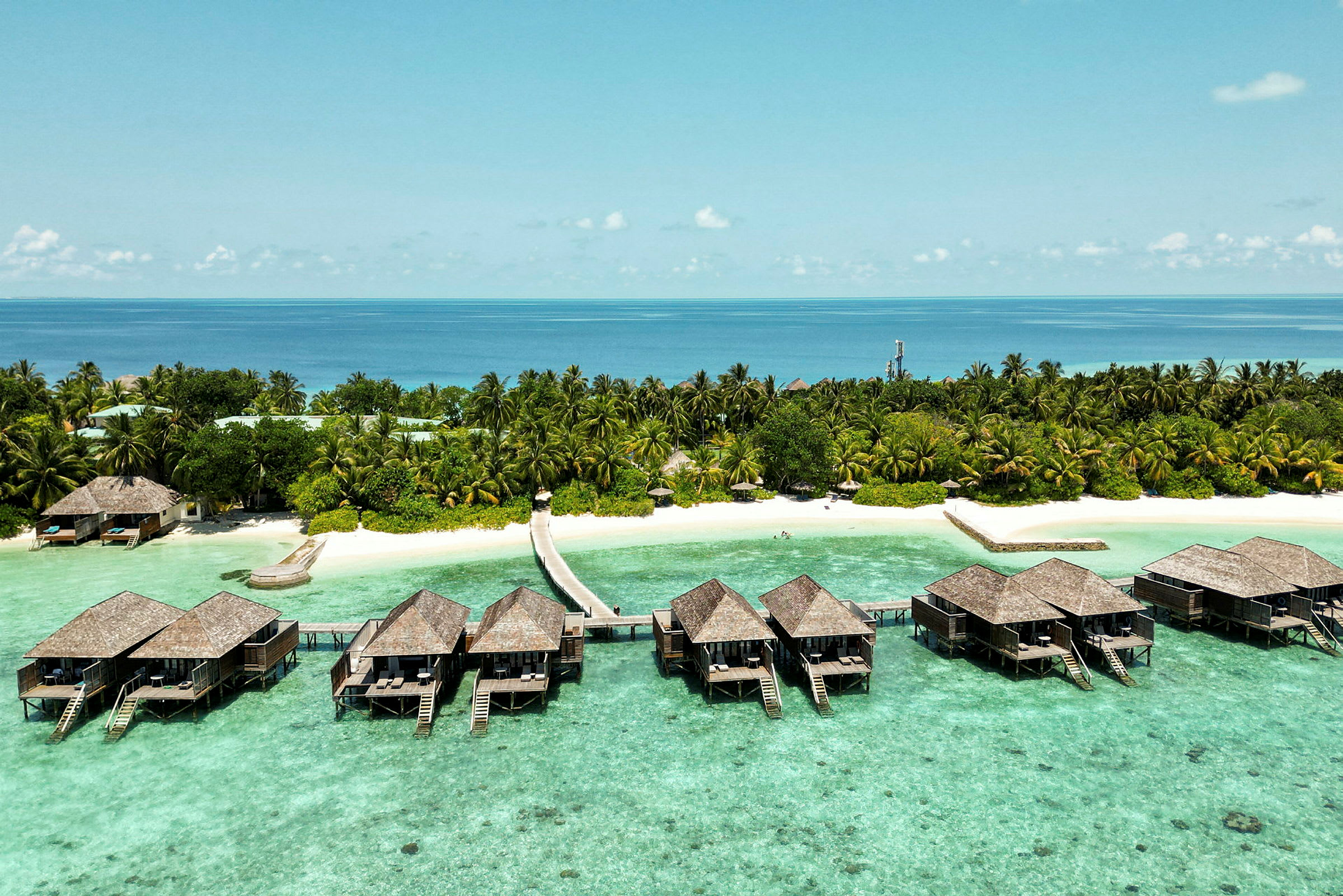 Luksuriøse bungalower på påler over klart turkist vann og en tropisk strand med palmer. (AI-generert tekst)