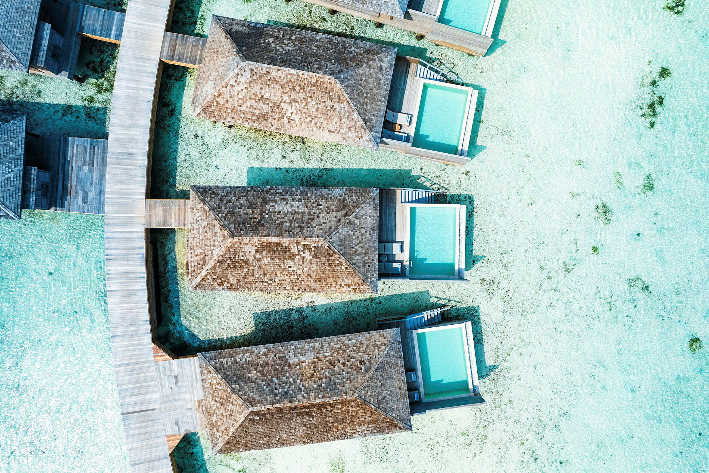 Luftfoto av strandvillaer med private bassenger bygget over klart vann, tilkoblet med trebroer. (AI-generert tekst)