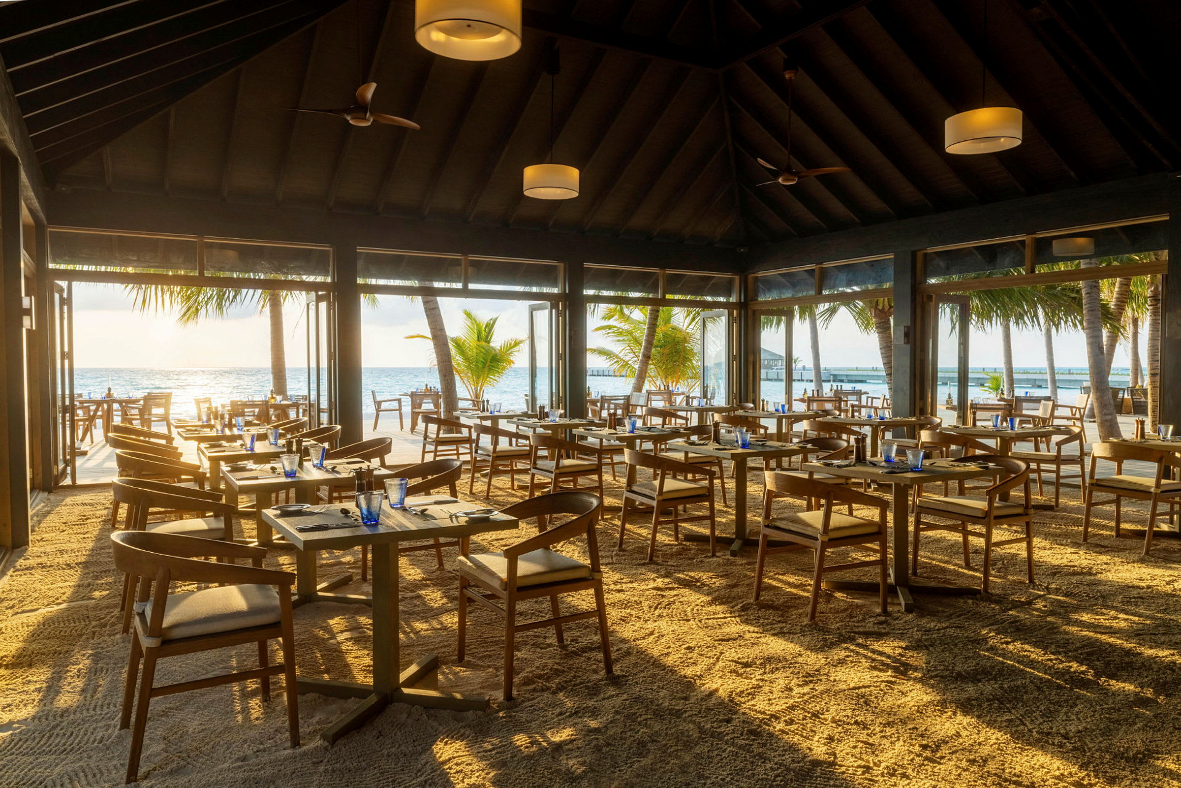 Restaurant med sandgulv og utsikt over havet og palmetrær. (AI-generert tekst)
