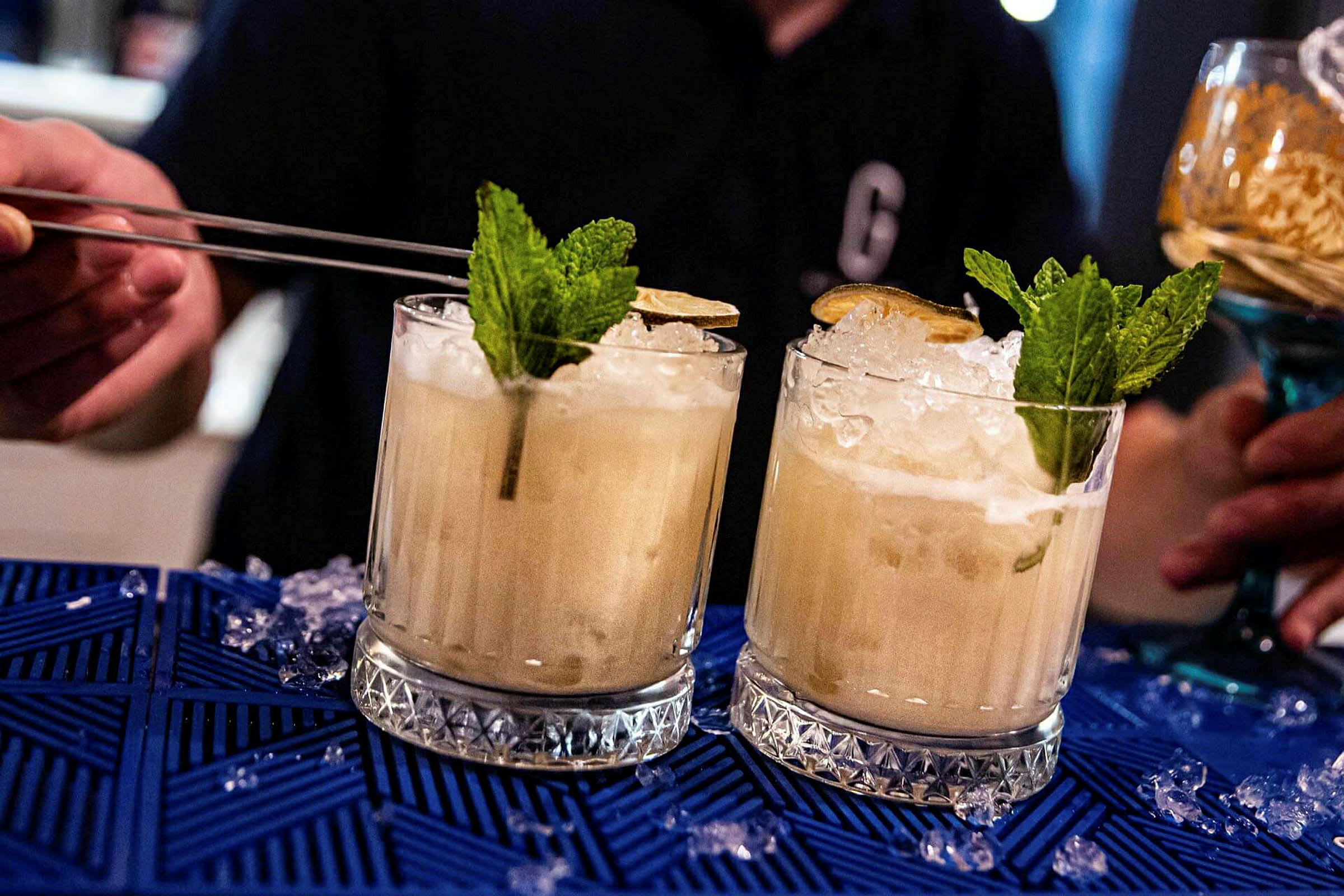 To cocktails med is, mynte og lime på blå duk. (AI-generert tekst)