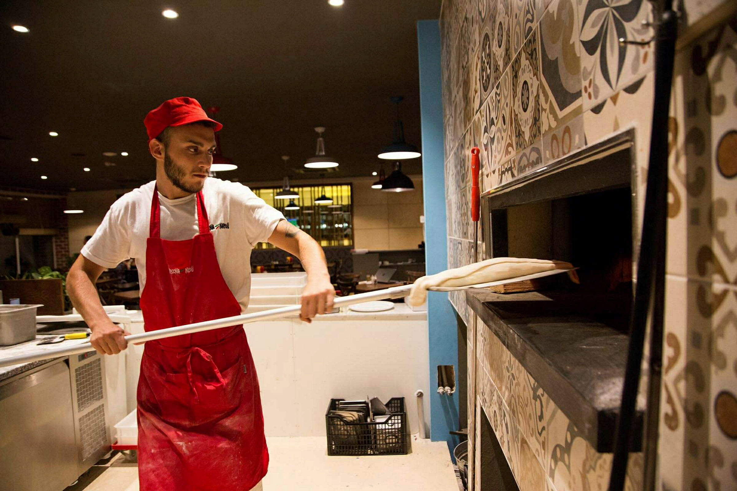 En kokk i arbeidstøy forbereder en pizza og plasserer den i en vedfyrt ovn. (AI-generert tekst)