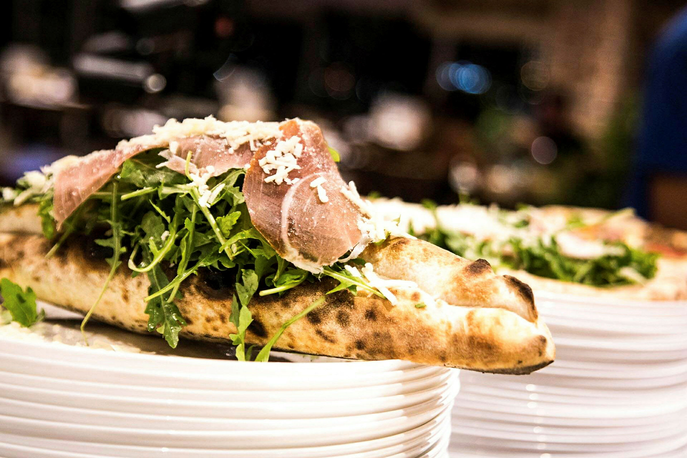 Et nærbilde av en pizza med ruccolasalat og skinke, toppet med revet ost, servert på en tallerken. (AI-generert tekst)