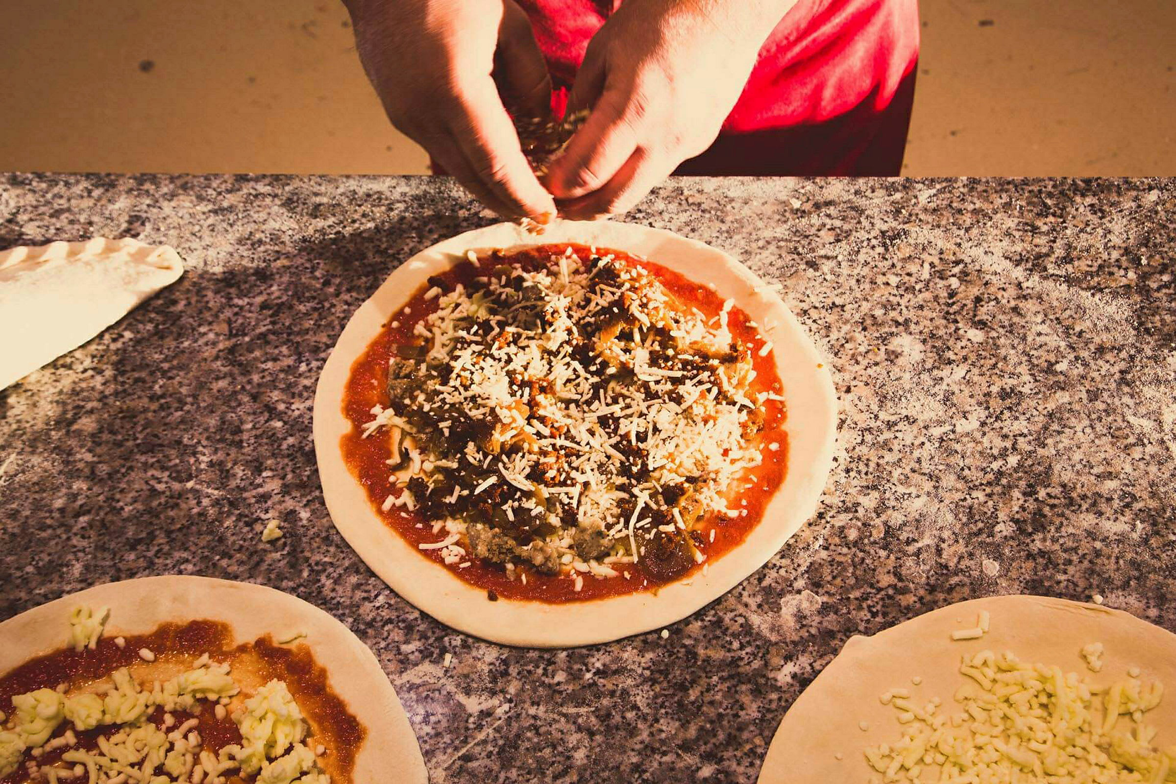 En person tilbereder en pizza med pålegg på en marmorbenk. (AI-generert tekst)
