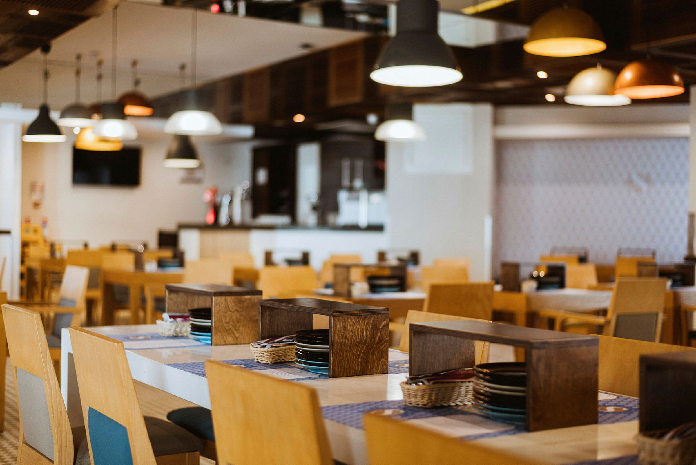Restaurant med trebord og stoler, opplyst av taklamper. (AI-generert tekst)