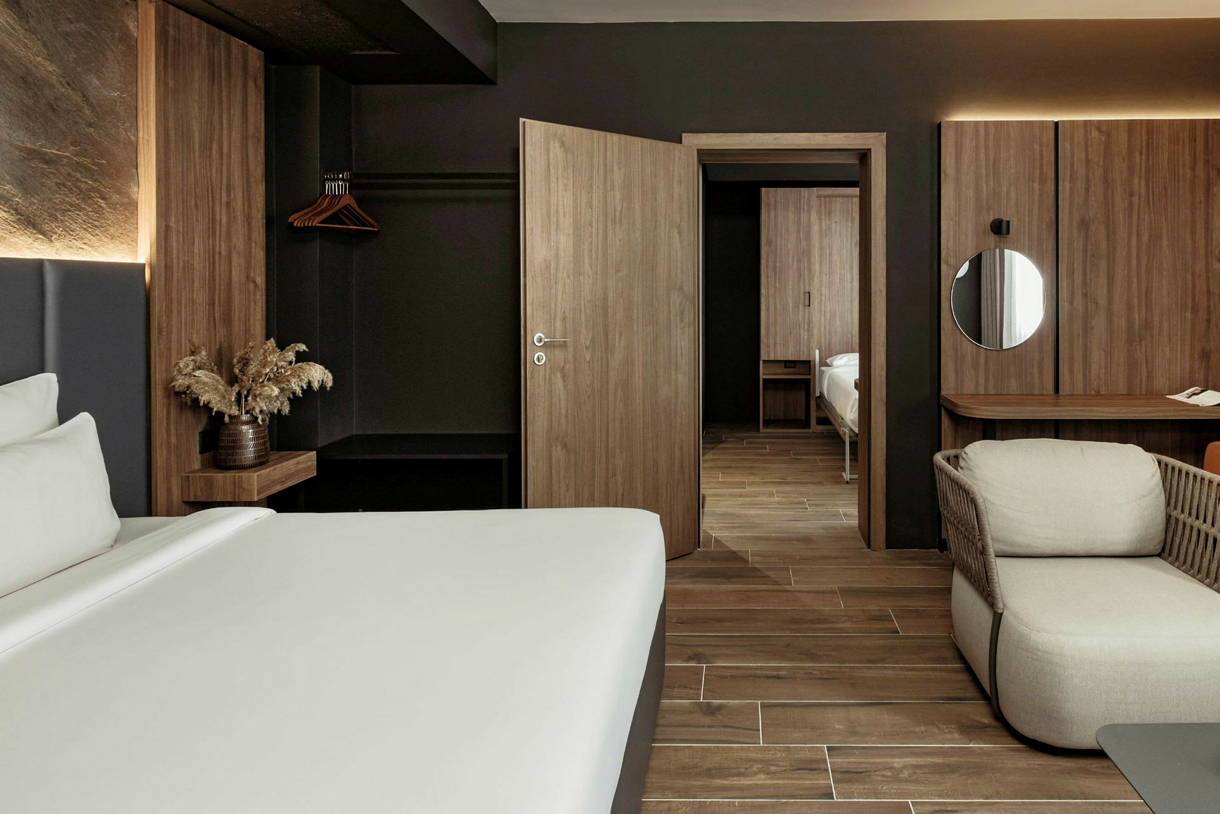 Et moderne hotellrom med mørke tremøbler og minimalistisk design. En seng, en lenestol og et skrivebord er synlige i rommet. (AI-generert tekst)