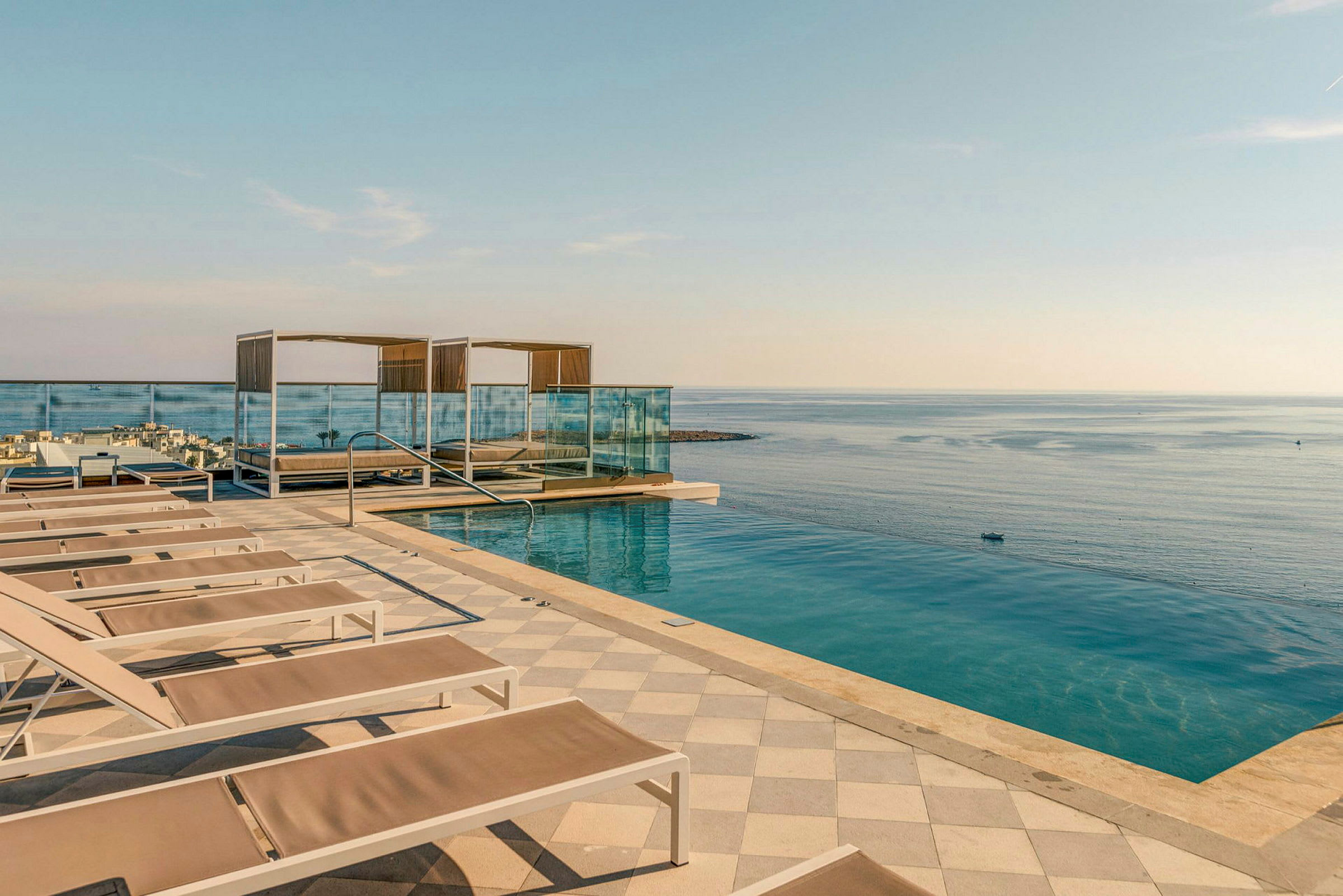 Et infinitybasseng ved havet med solsenger og skyggefulle cabanas, samt et rekkverk mot vannet. (AI-generert tekst)
