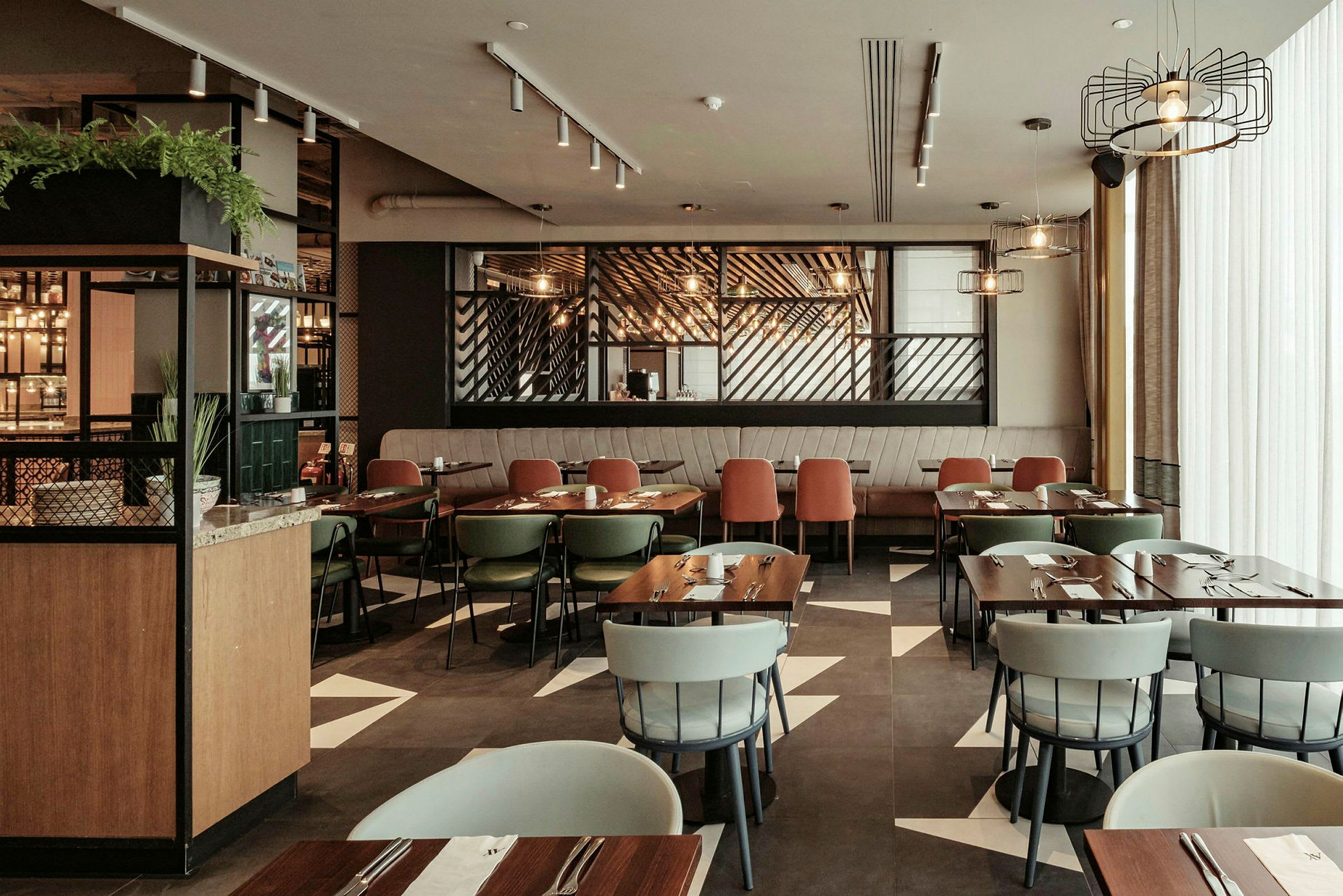 Et moderne innredet restaurantområde med flere bord og stoler, belysning og dekorative elementer. (AI-generert tekst)
