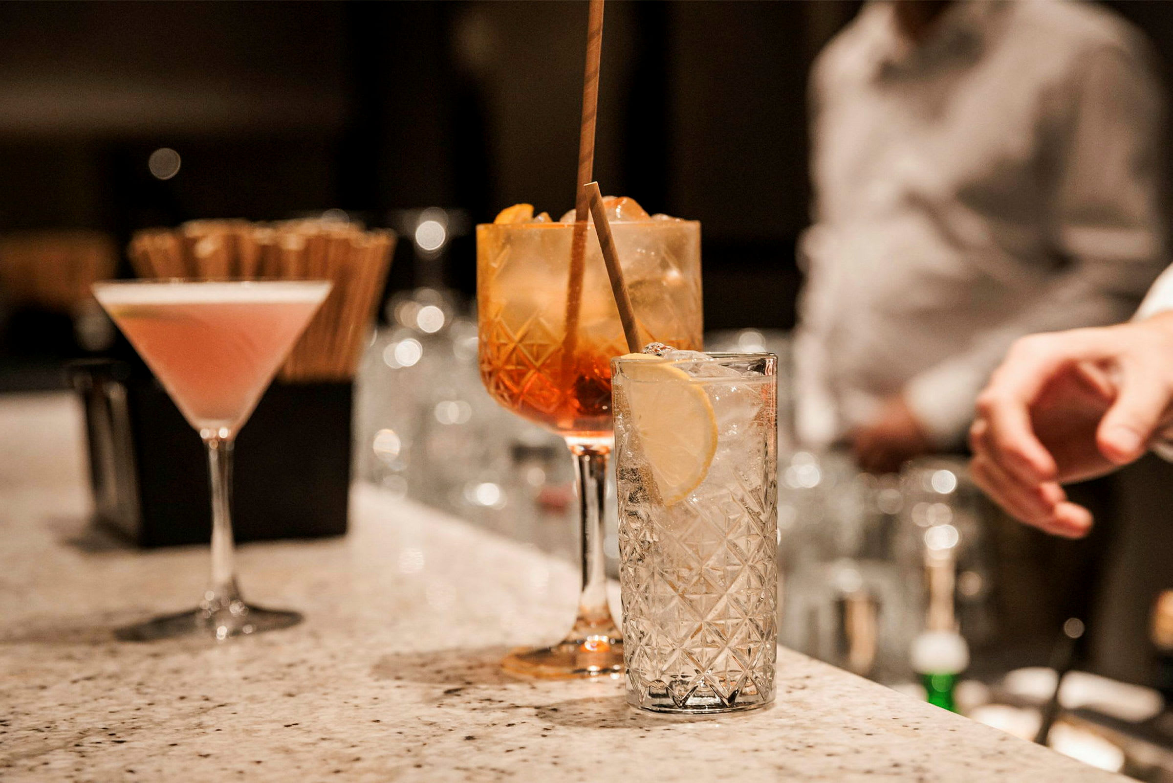 Flere glass med ulike cocktails står på en bardisk i marmor. (AI-generert tekst)