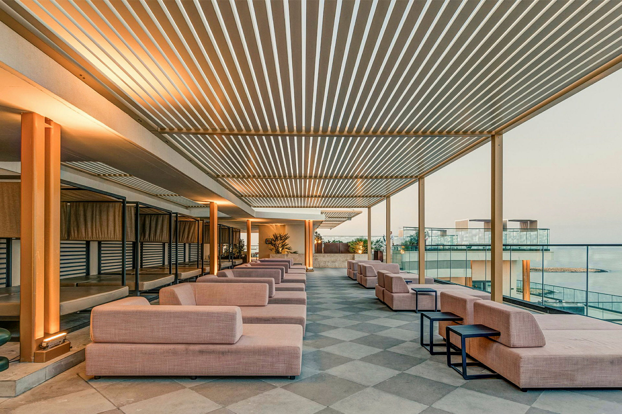 Et moderne takterrasseområde med brede sofaer og bord, omgitt av åpne områder og glassrekkverk. (AI-generert tekst)