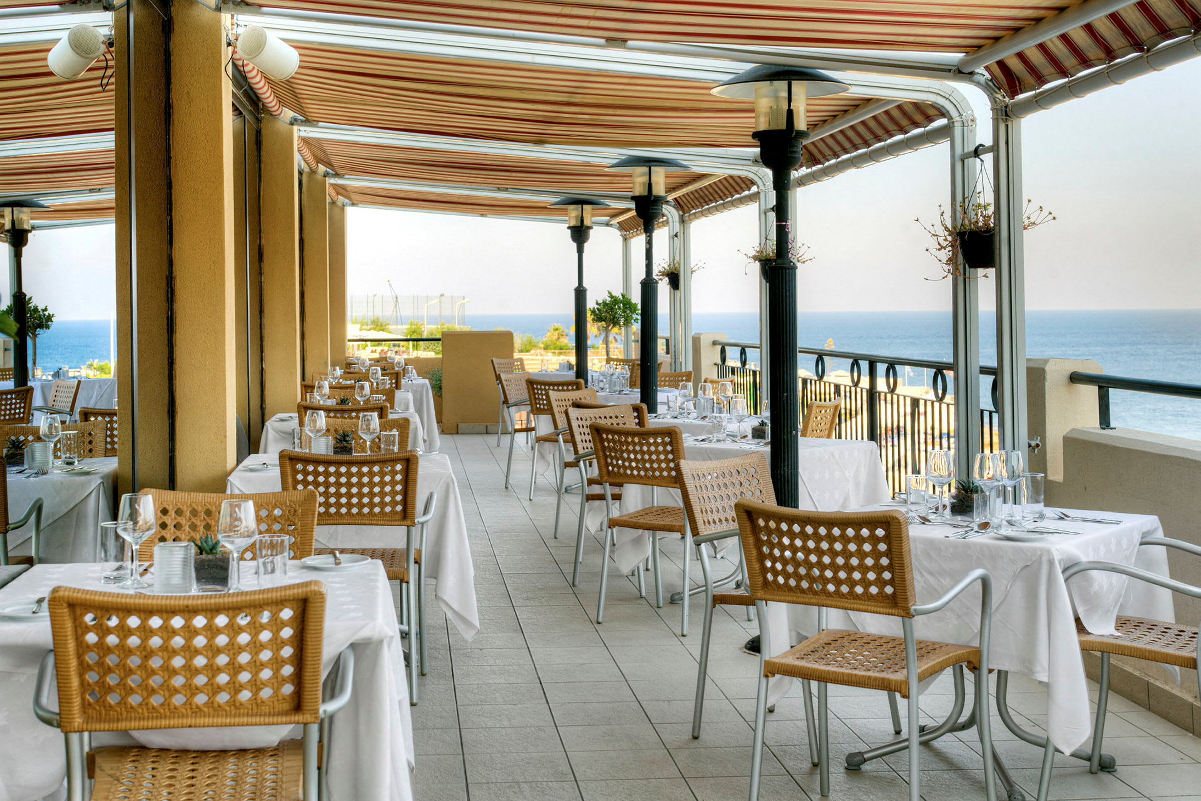 En restaurantterrasse med dekkede bord og utsikt over havet. (AI-generert tekst)