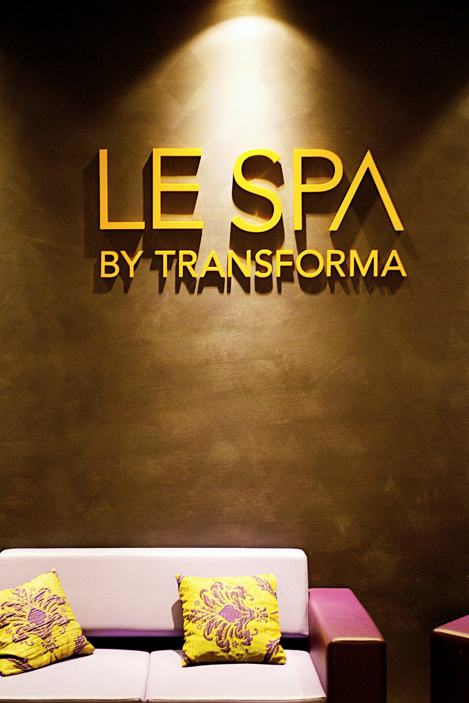 Bilde av en spa-inngang med teksten "Le Spa by Transforma" på veggen. En sofa med fargerike pynteputer er synlig. (AI-generert tekst)