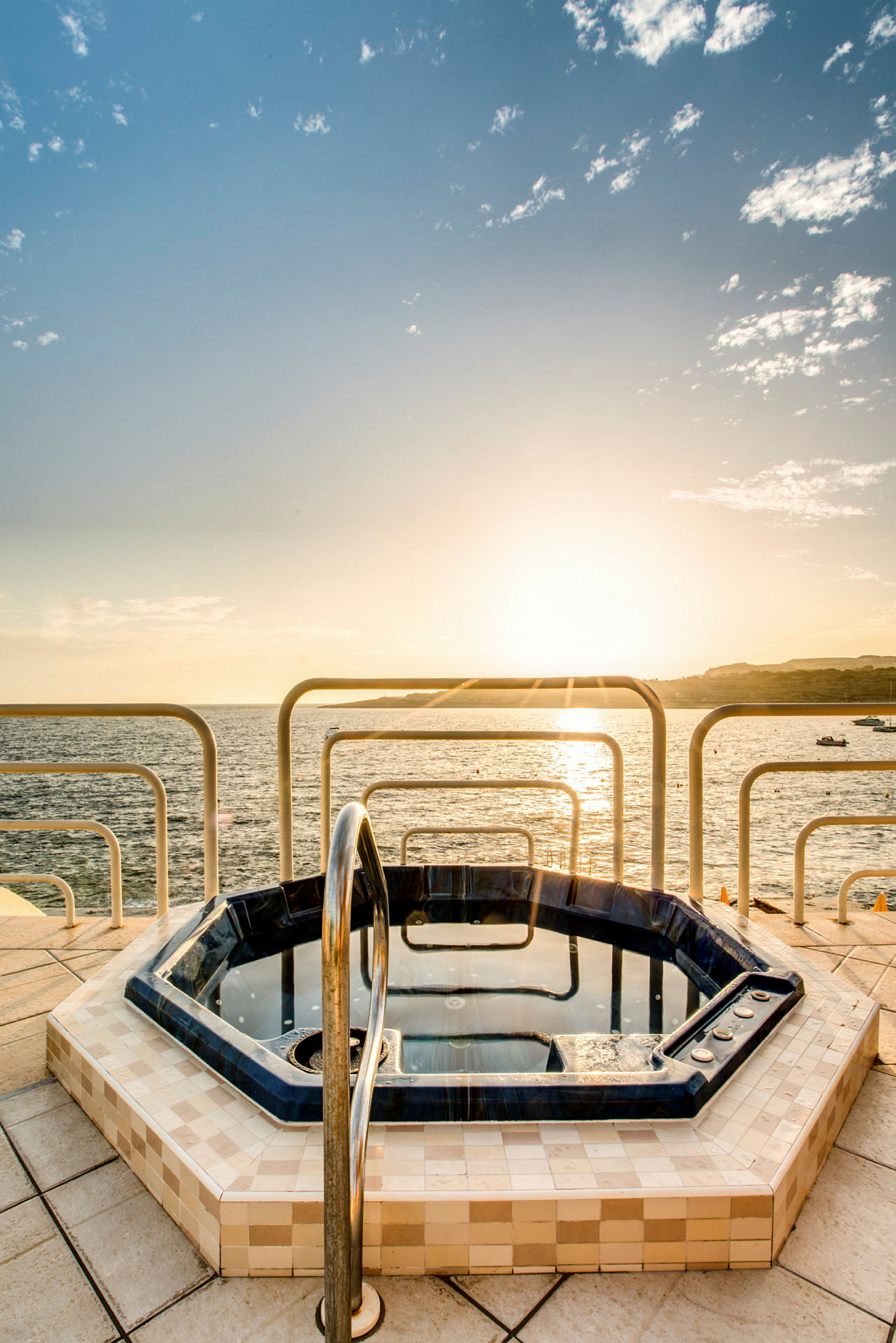 Et boblebad på en terrasse med utsikt over havet og en solnedgang. (AI-generert tekst)
