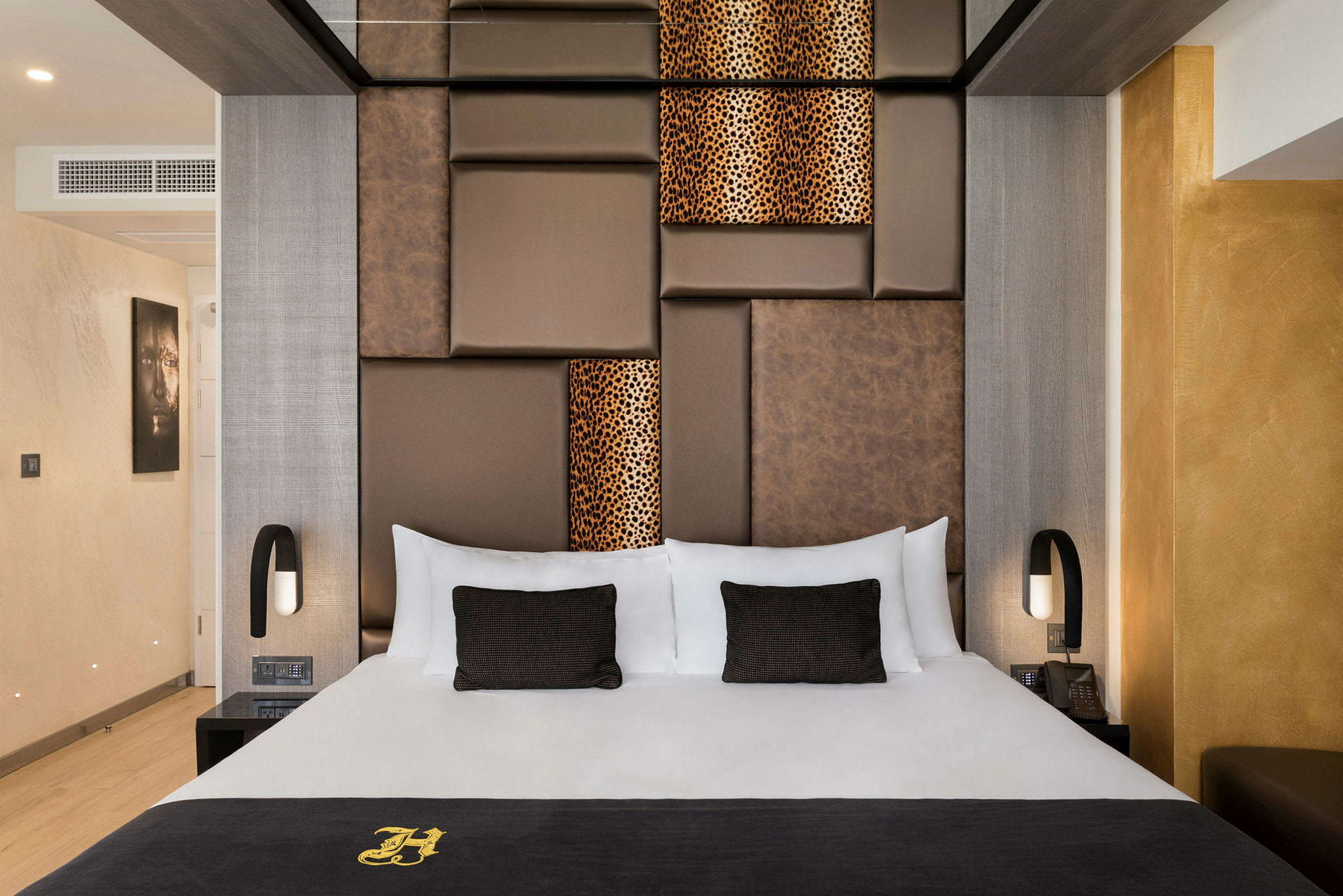 Et elegant hotellrom med en stor seng, med brune og mønstrede paneler på veggen bak. Rommet er moderne innredet med varme farger. (AI-generert tekst)