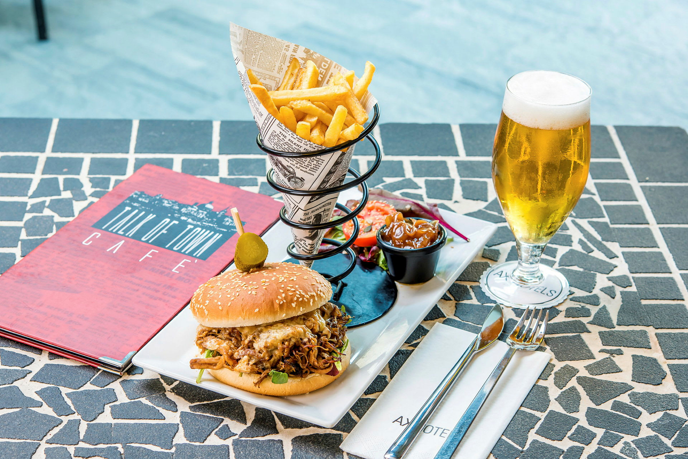 En tallerken med en hamburger, pommes frites, salat, saus og et glass med øl på et bord. (AI-generert tekst)
