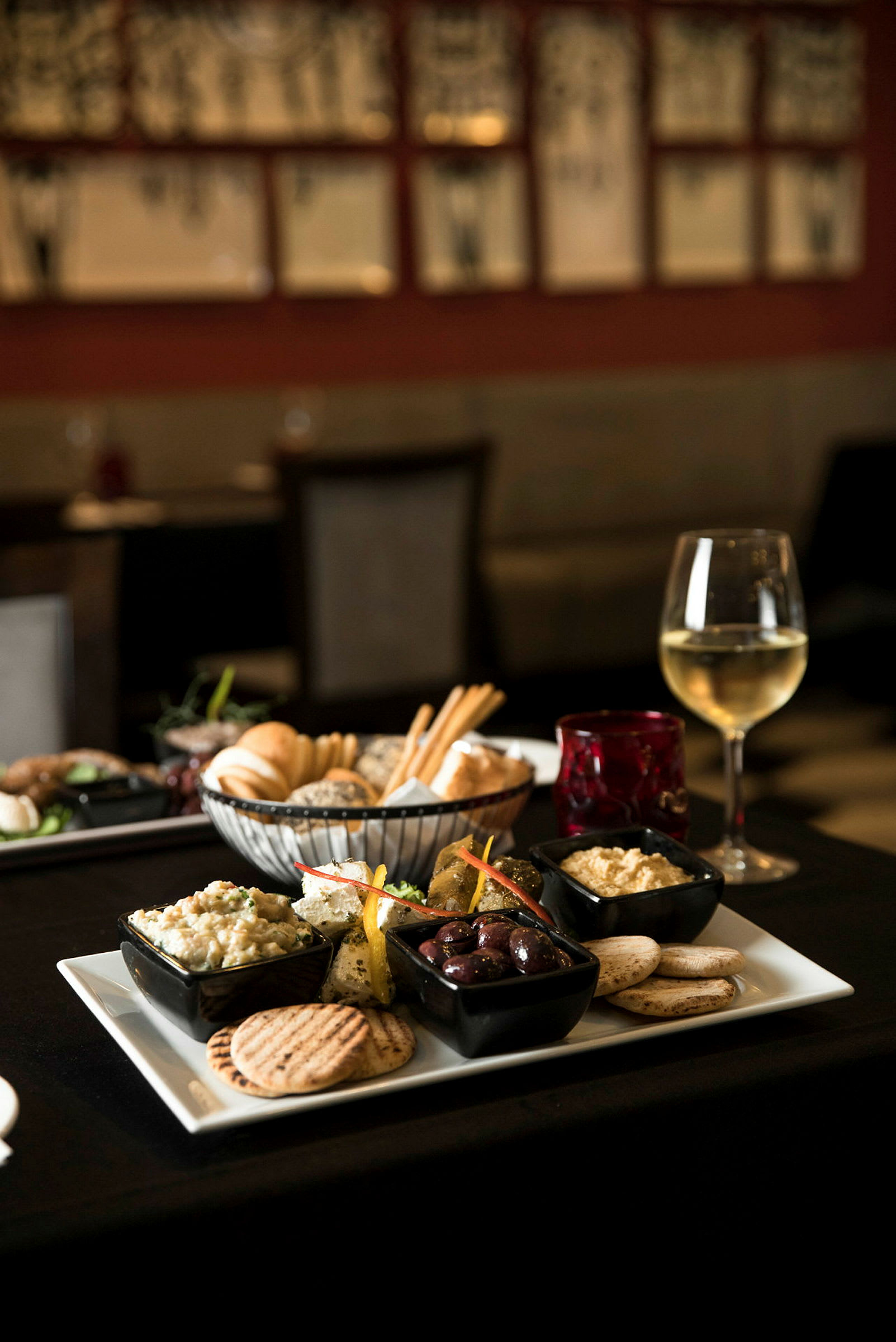 Et fat med forskjellige småretter, inkludert oliven, hummus og brød, serveres sammen med et glass hvitvin. (AI-generert tekst)