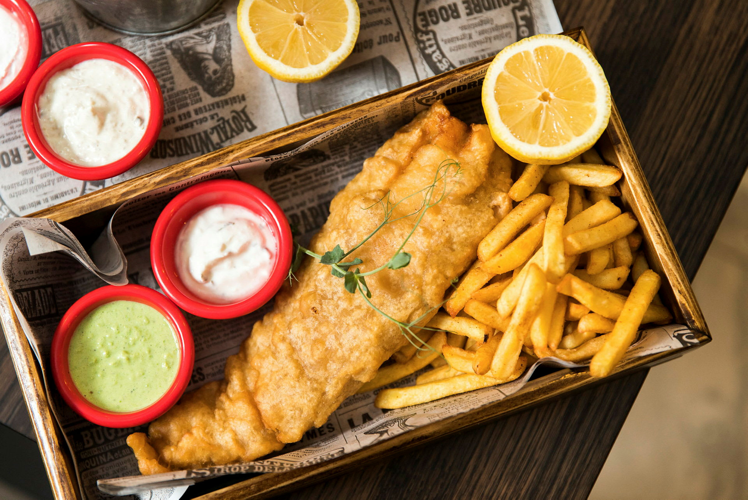Fish and chips servert med sauser og sitronhalvdeler. (AI-generert tekst)