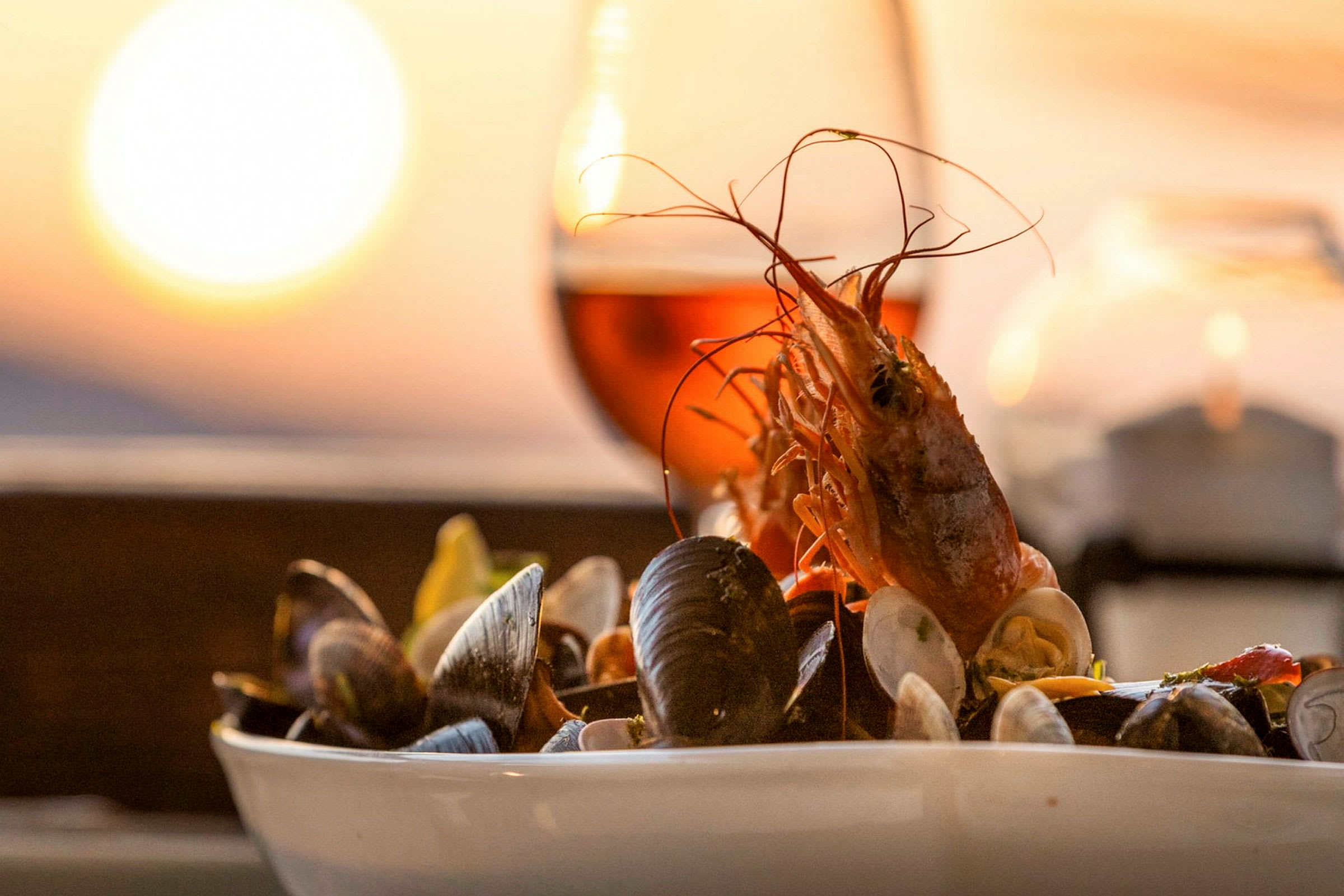En tallerken med skalldyr ved solnedgang med et glass vin i bakgrunnen. (AI-generert tekst)
