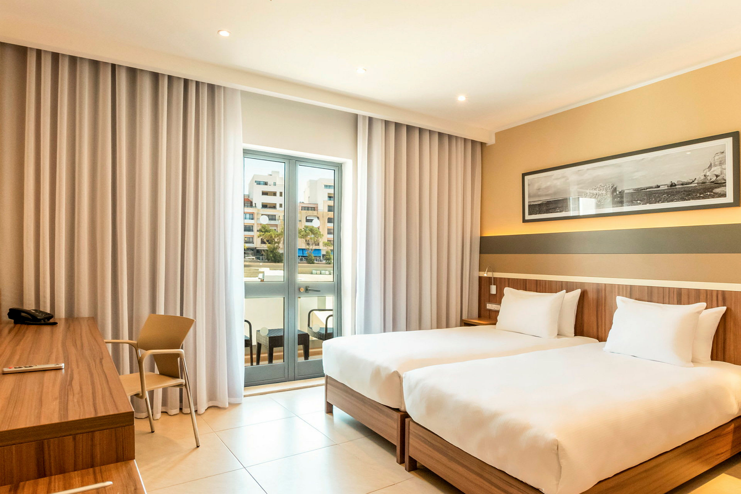 Hotellrom med to enkeltsenger, skrivebord og en balkong med glassdører. (AI-generert tekst)