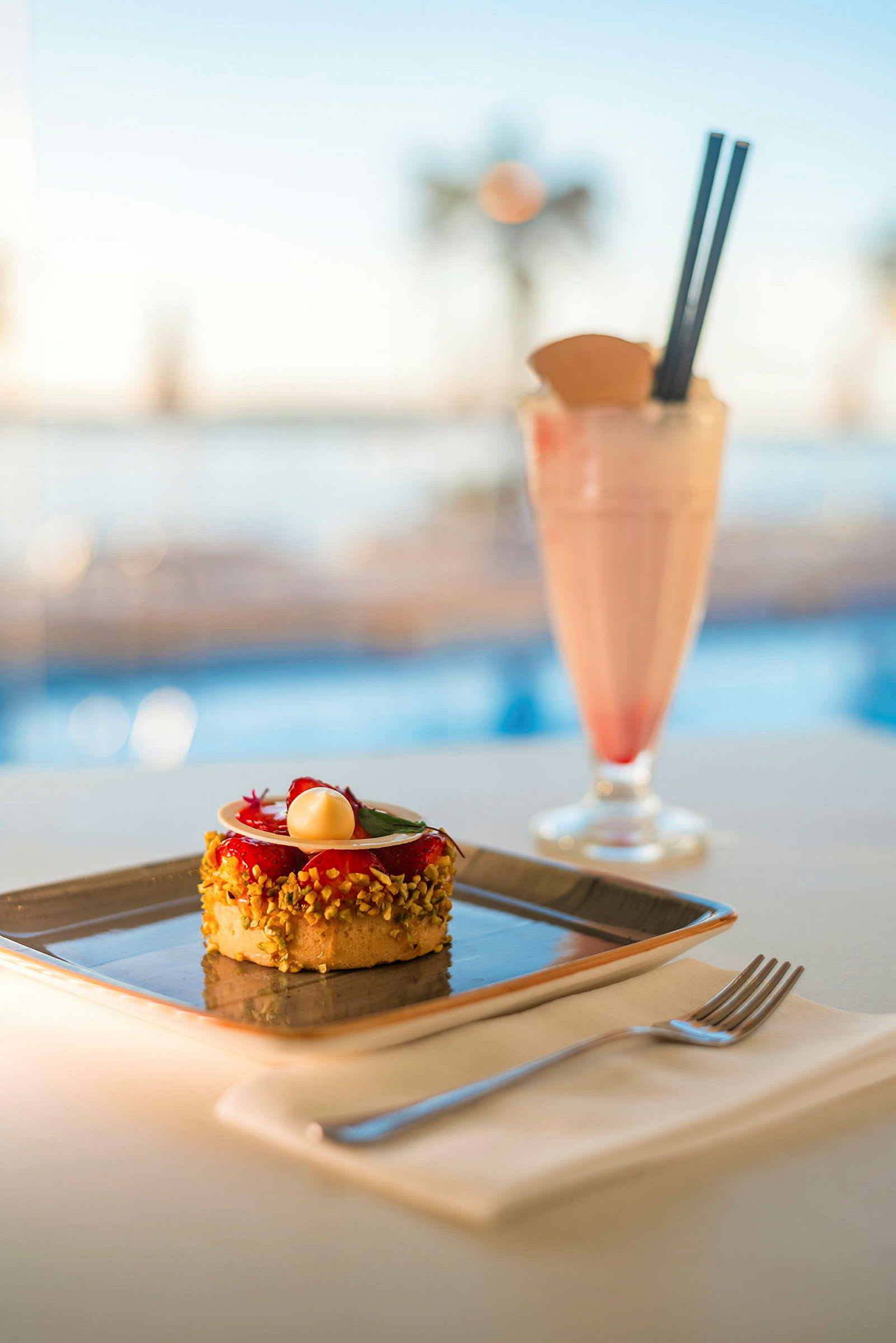 En dessertkake servert på en firkantet tallerken ved siden av et rosa milkshakeglass på et bord. (AI-generert tekst)